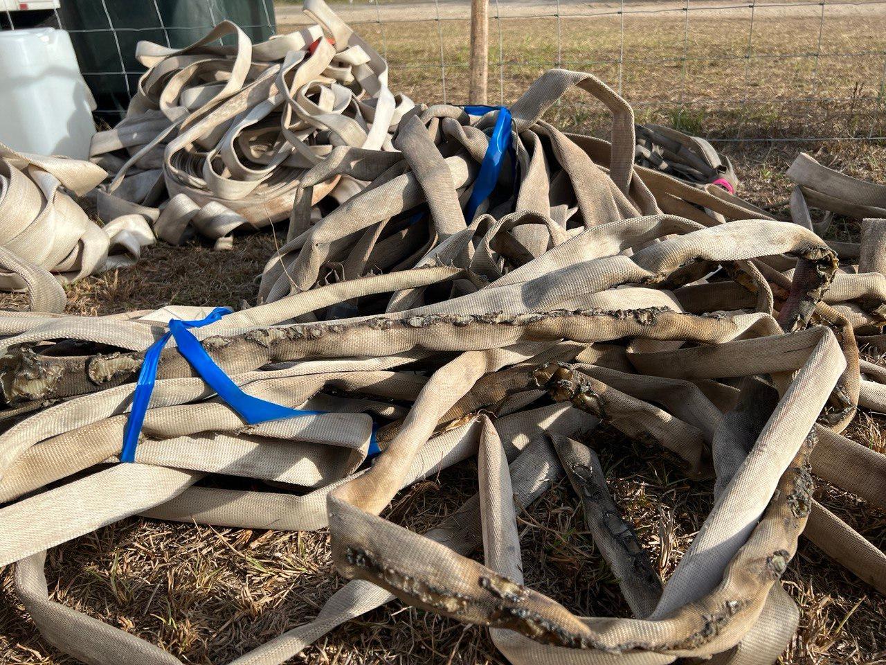 Piles of white hose lays on ground. Hose in foreground has multiple brun and melted spots from damage on the fire line