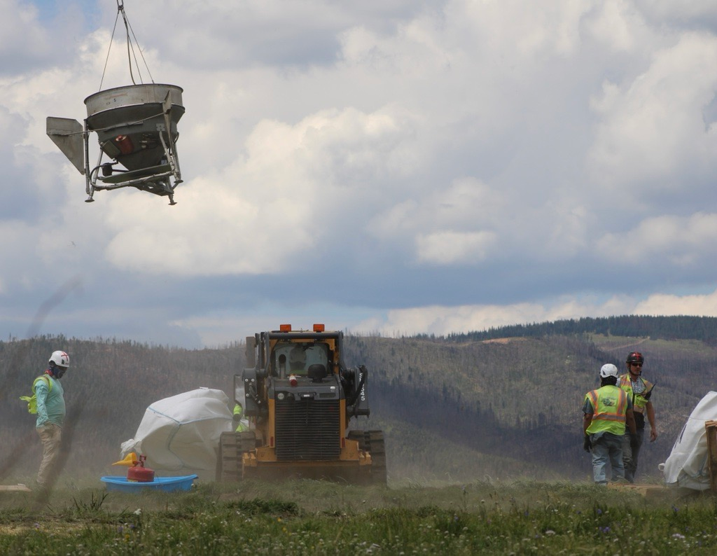 Image of the spreading bucket  hanging  in the air  with crews and heavy equipment on the ground.