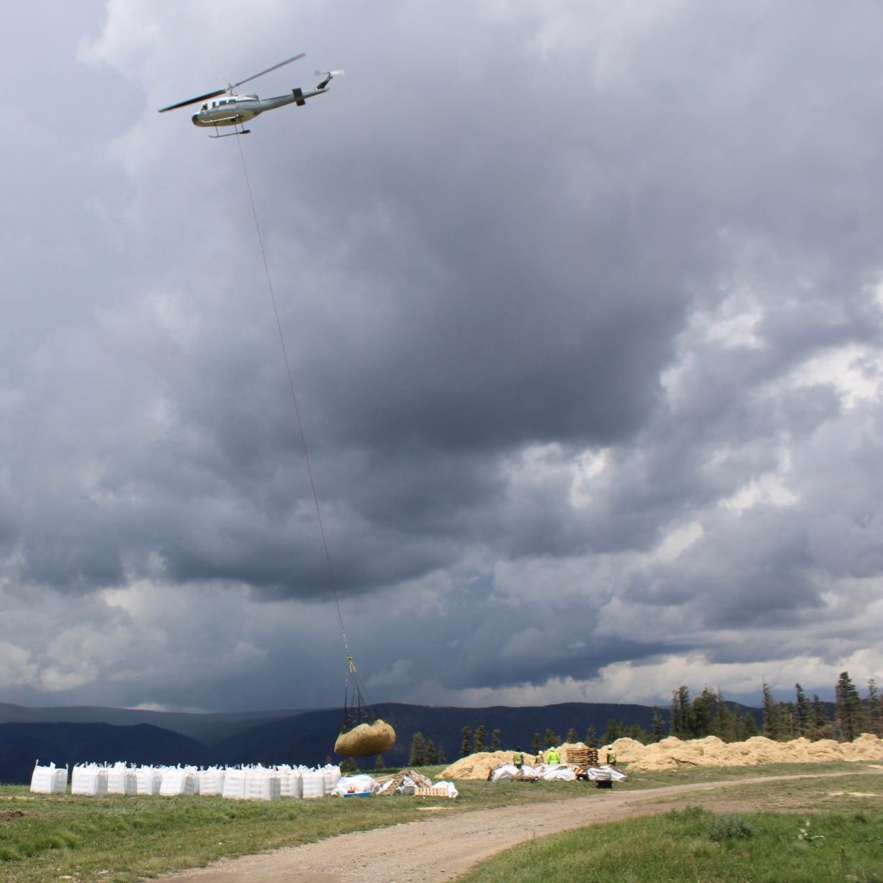 Image of helicopter lifting off with hanging net of straw mulch.