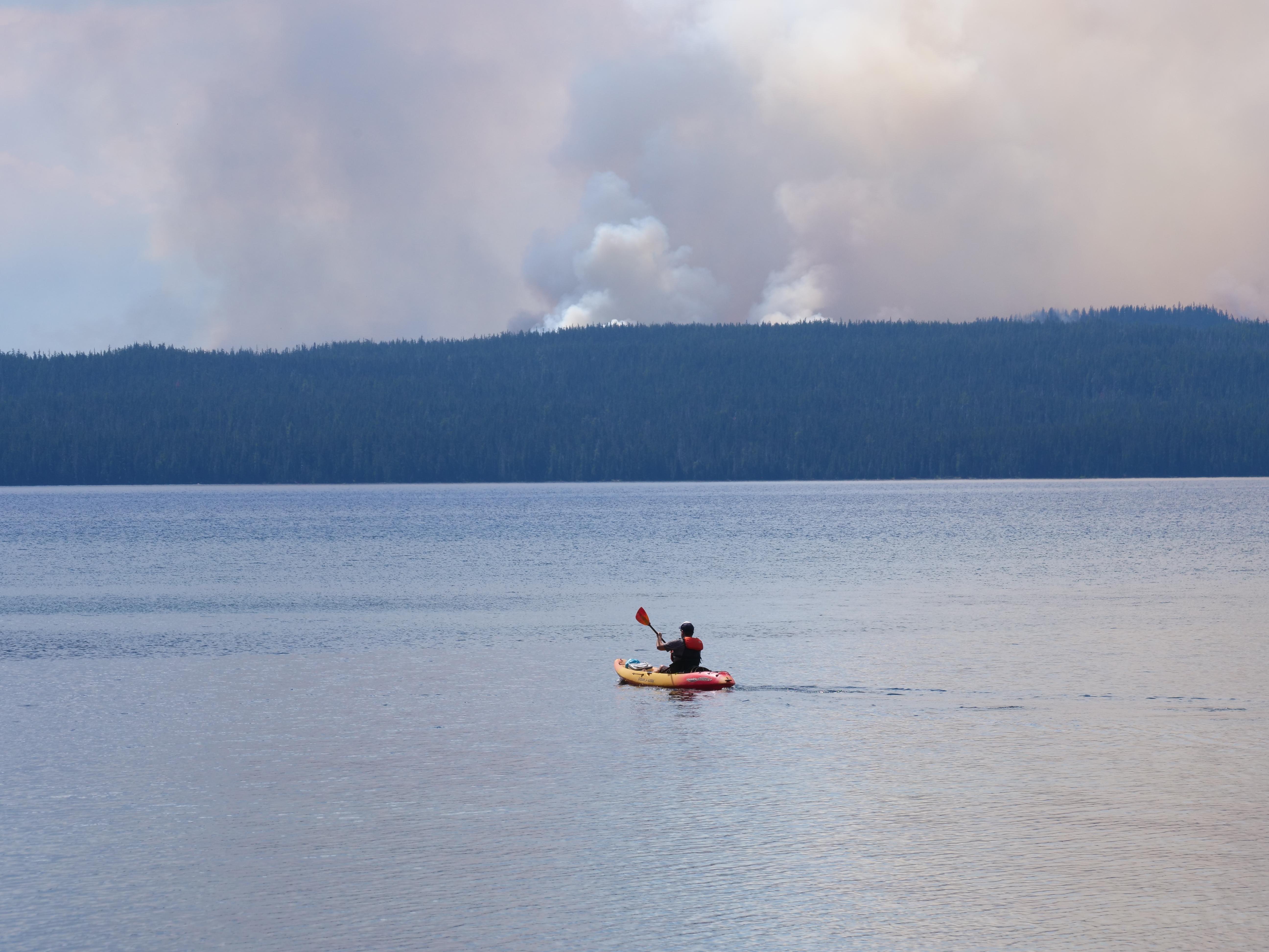 Kayaker shown on Waldo Lake with prominent smoke column in the background.