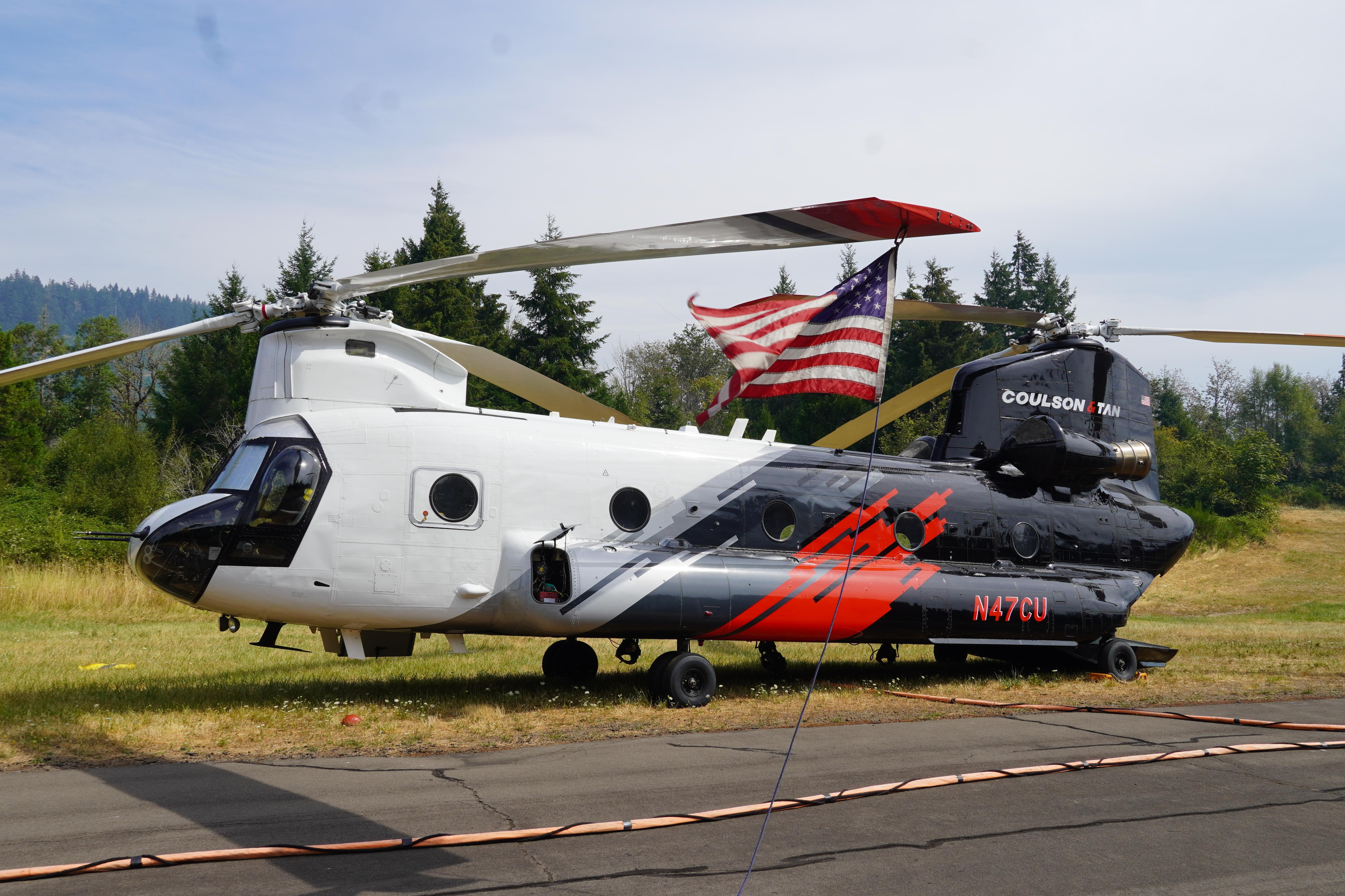 A red, white and blue, twin-rotor helicopter is shown sitting stationary. A US flag is mounted between the rotors.