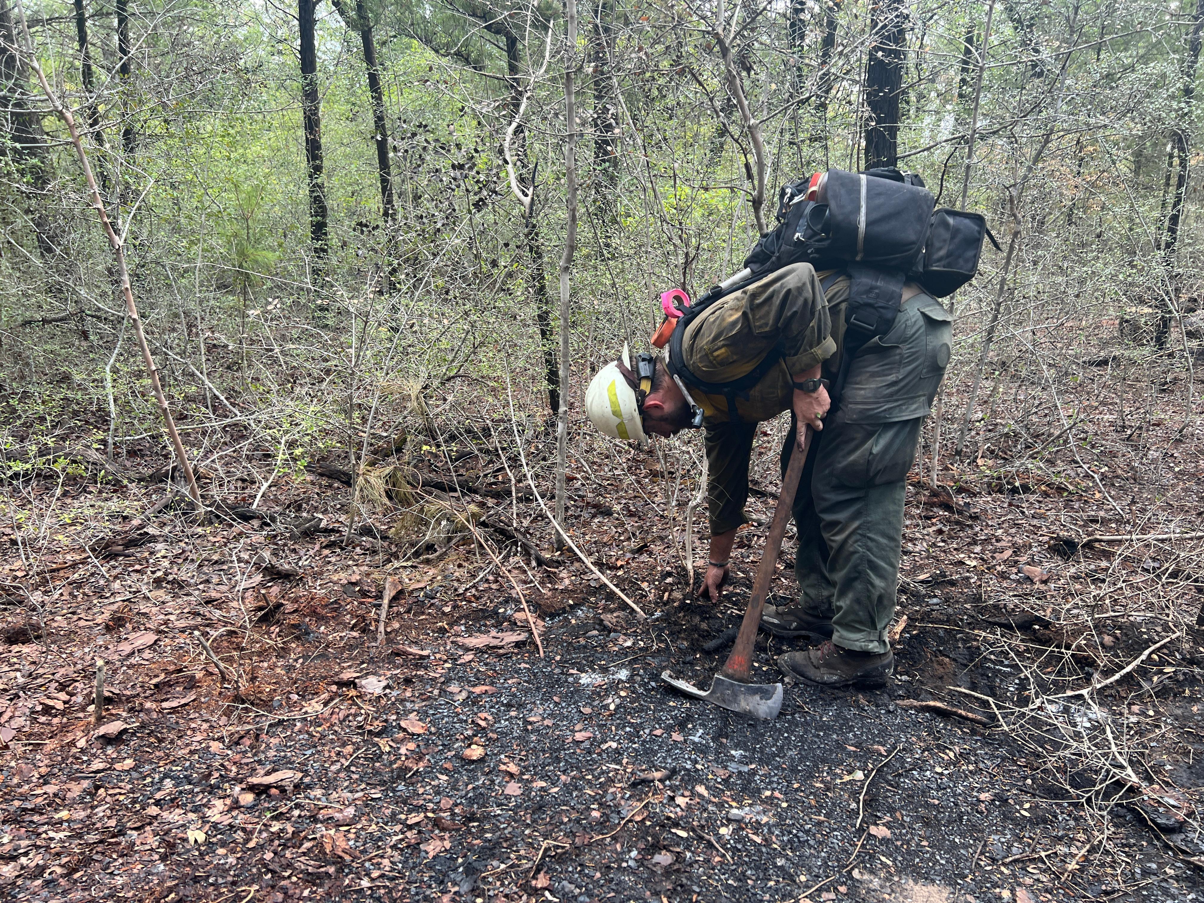 A single firefighter bends over to touch the black, burned ground to check for heat with a bare hand.