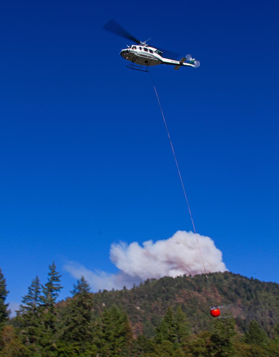 A helicopter flies in front of a large smoke plume.