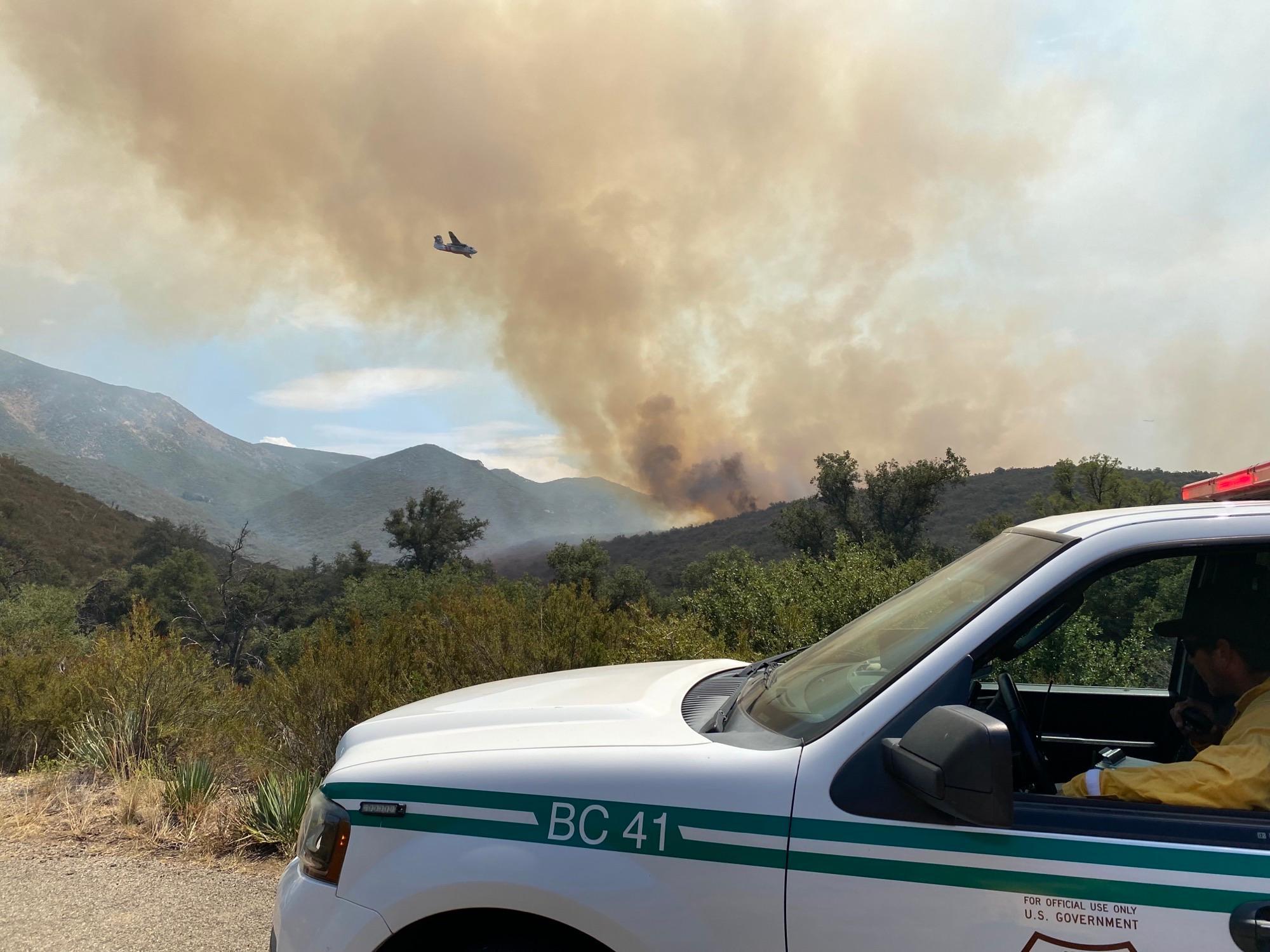 Smoke and an aircraft in the background of a parked forest service fire chief's vehicle