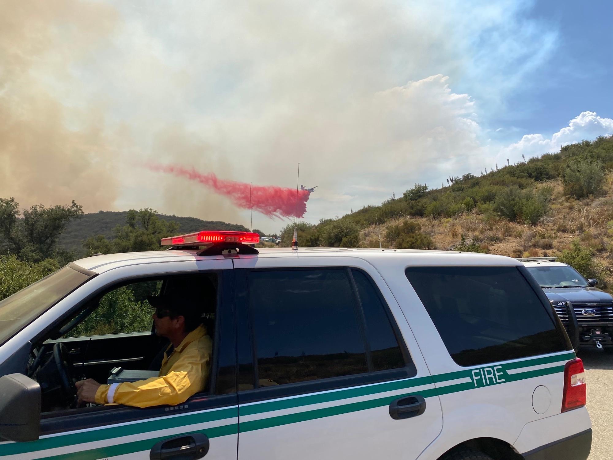 Airtanker dropping fire retardant on a hillside with a forest service fire chief's vehicle in the foreground