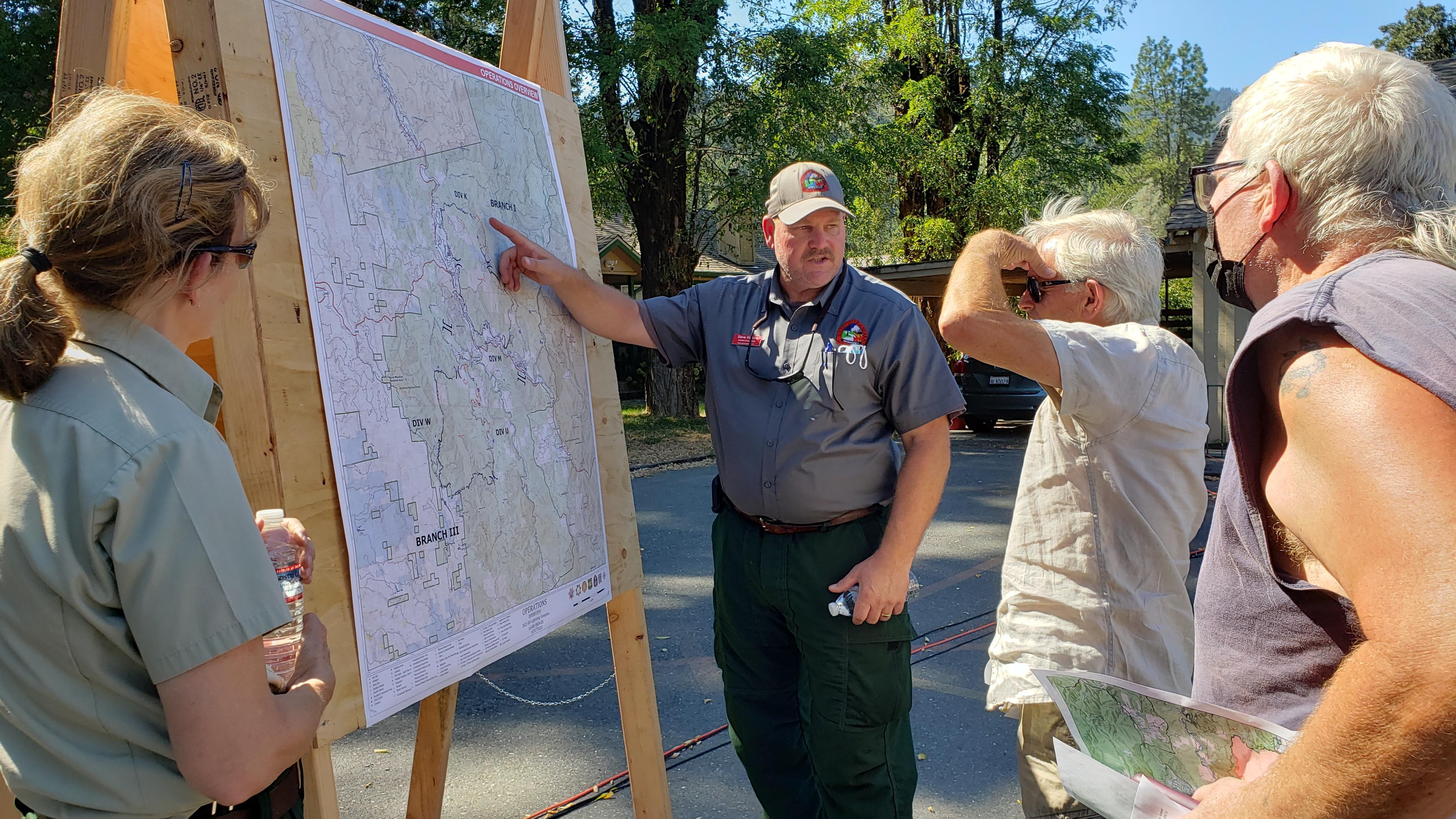 Two residents look at a map posted on a board with a member of CAIIMT14