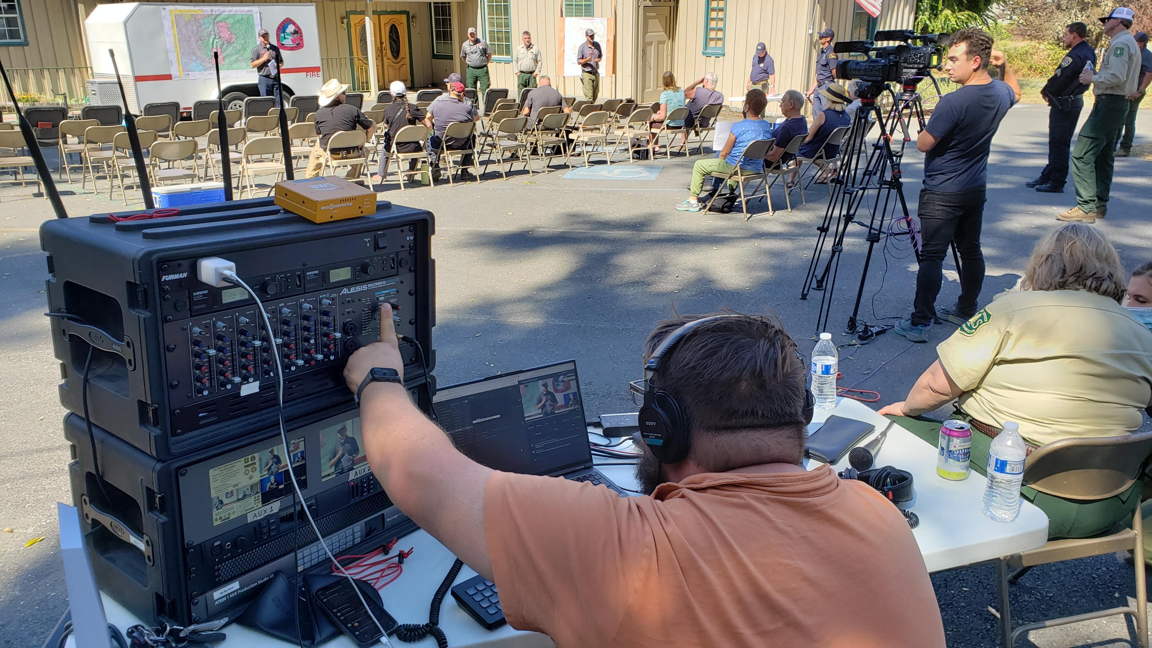 A member of a video production company uses equipment to broadcast a community meeting for CAIIMT14 to Facebook Live