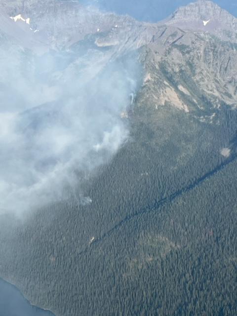 Smoke rises from the forested slope of Logging Mountain with the south edge of Quartz Lake in the foreground