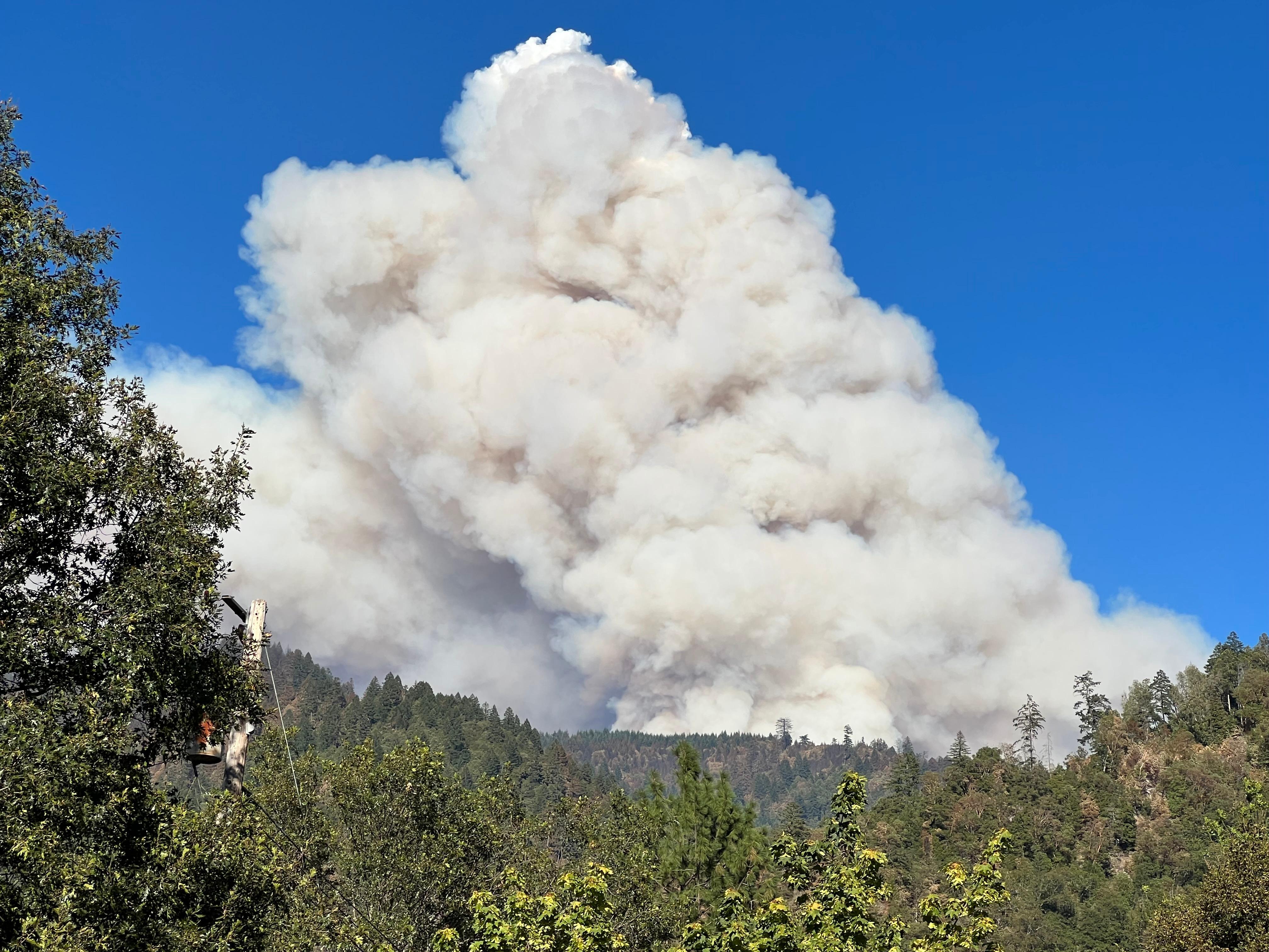 A large plume of smoke rises over mountains