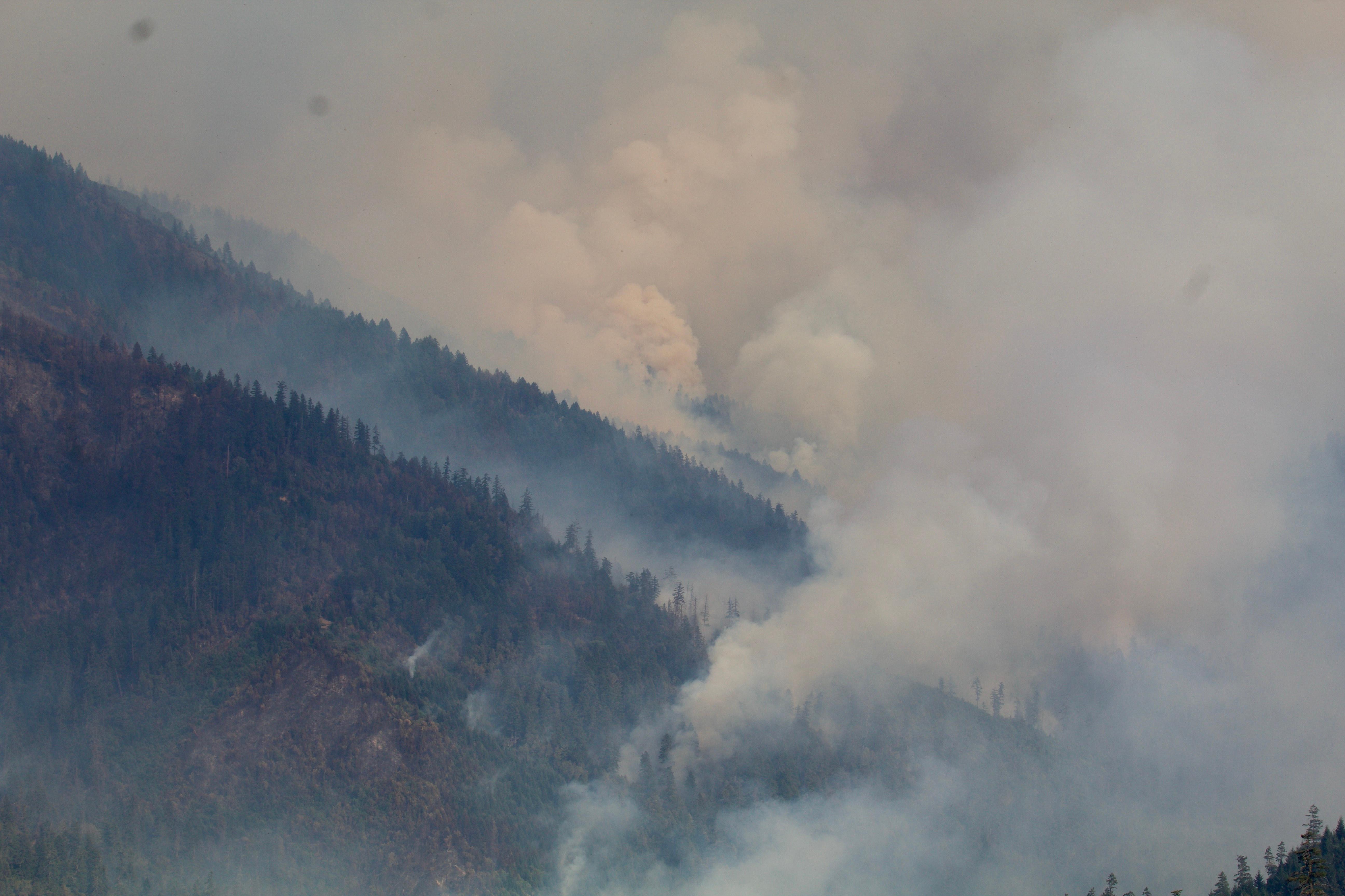 Smoke rises in multiple plumes from a valley surrounded by green hills