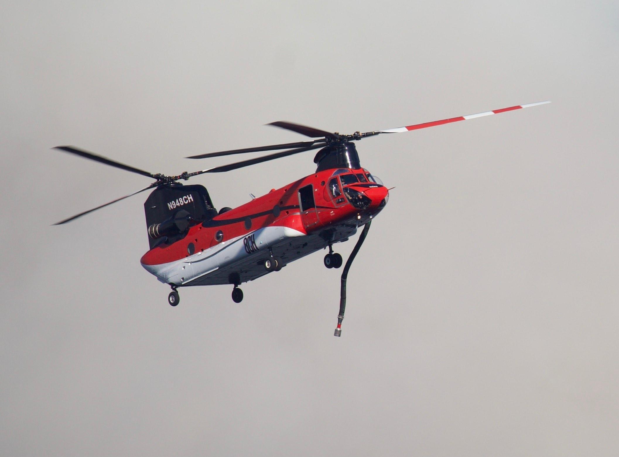 A red and white helicopter with two propellers flying in a smokey sky