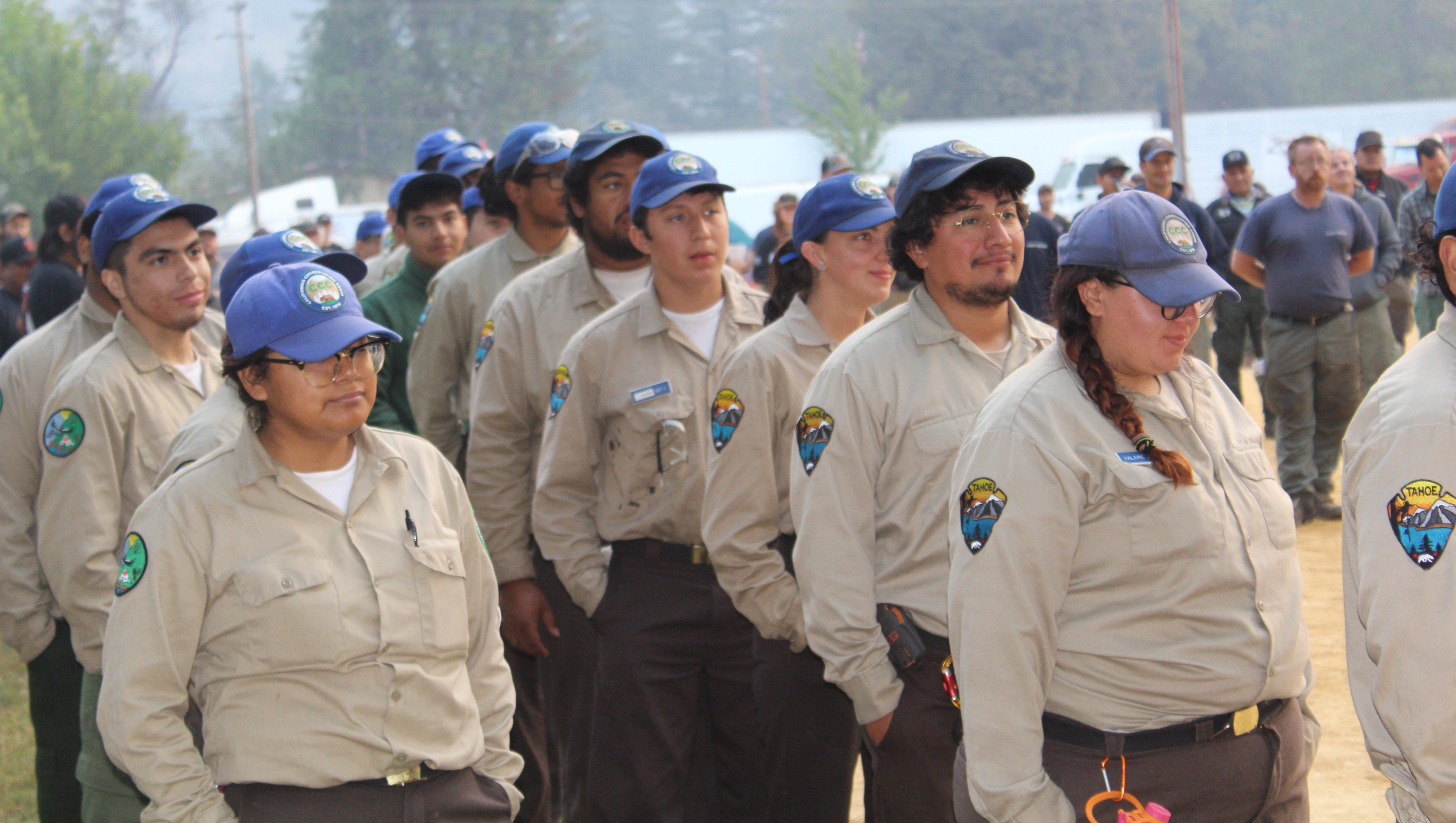 Young men and women in tan shirts and blue hats standing in an orderly group