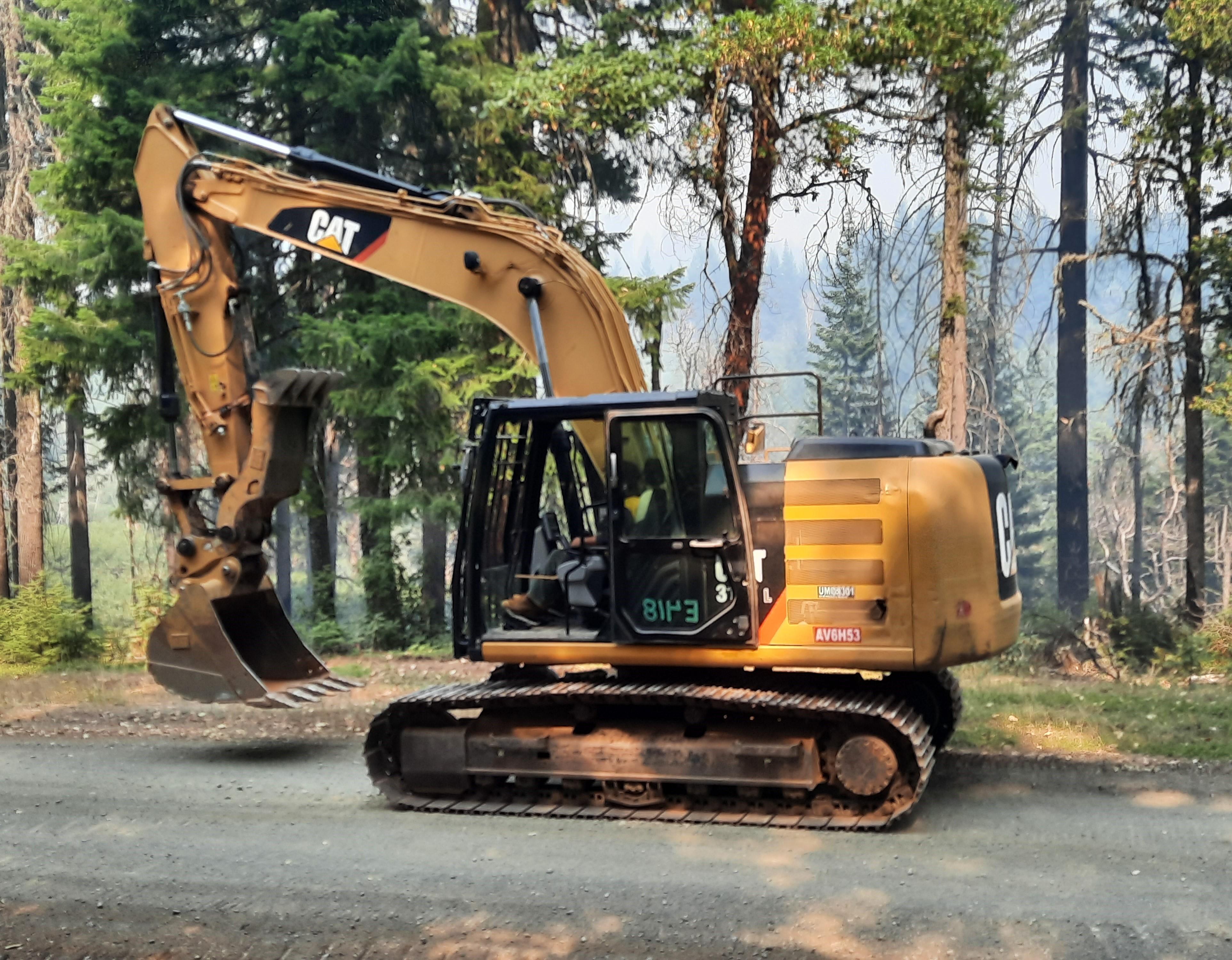 A yellow and black excavator operating on a paved road through the forest