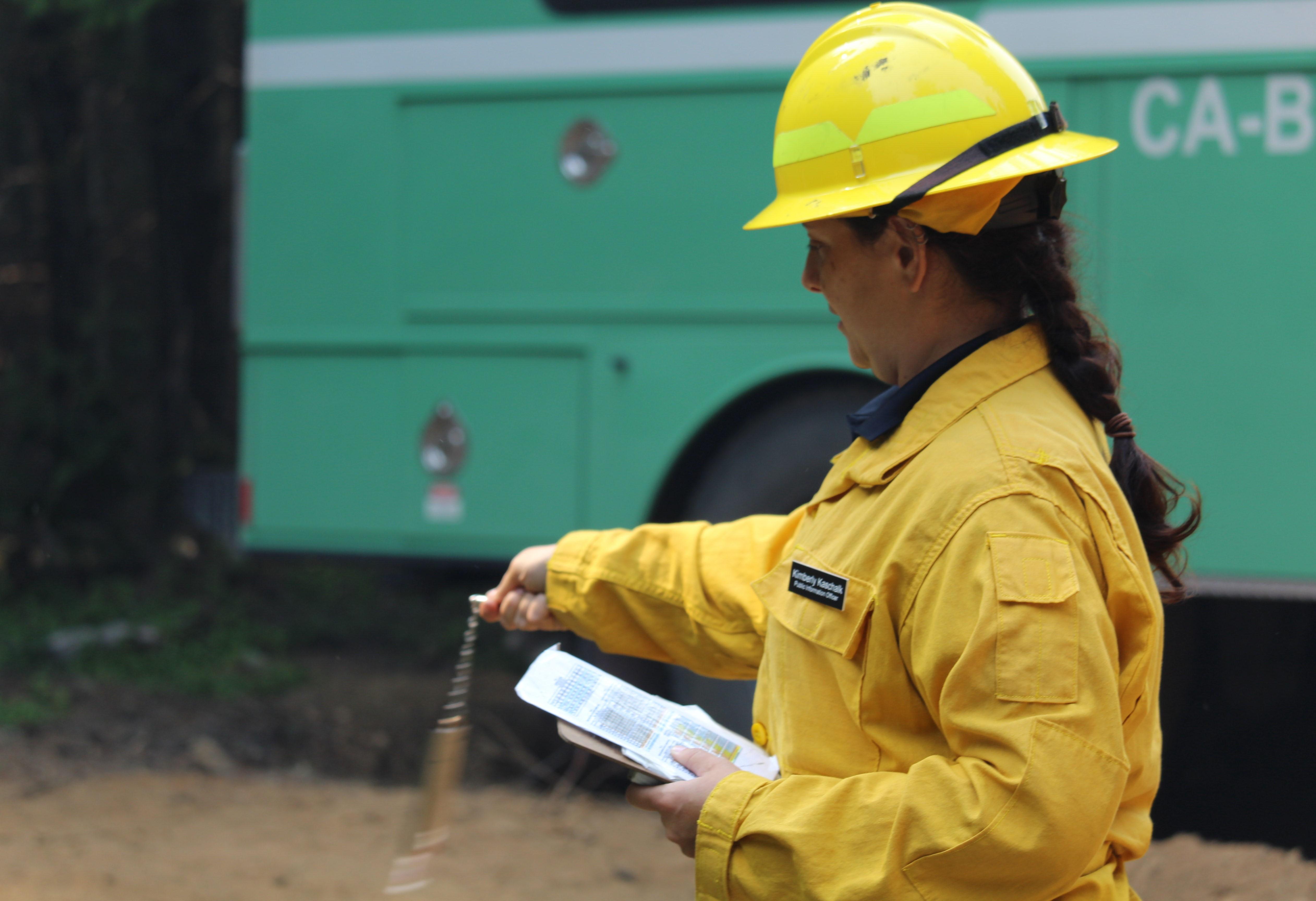 A female firefighter uses specialized equipment to measure weather while standing near a green truck in a forest