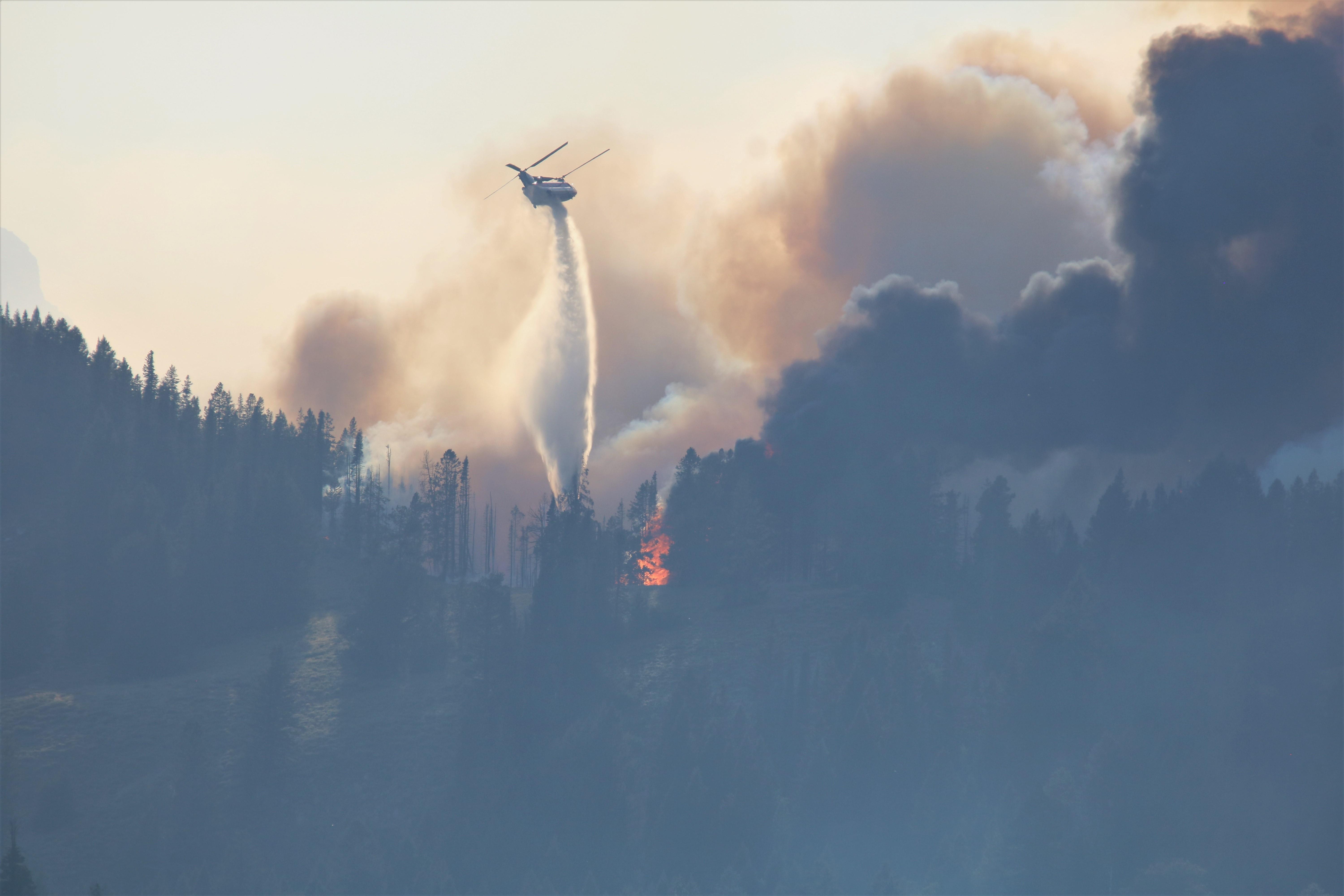 A helicopter drops water on flames in the trees.