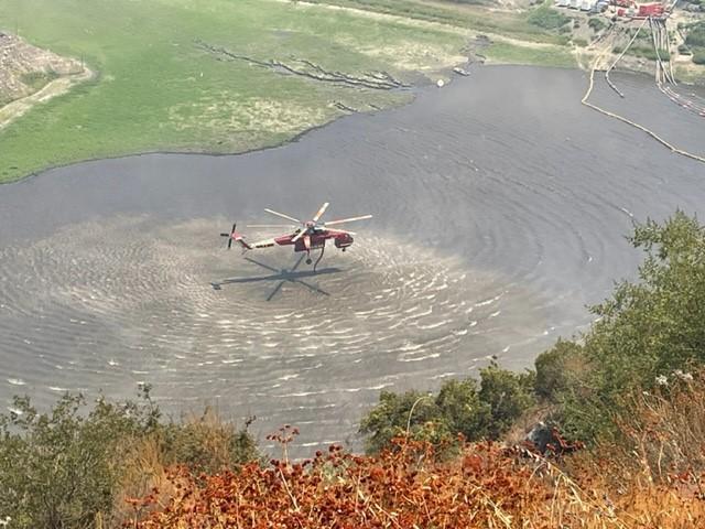 Helicopter pulls water from dam site to help put out fire elsewhere.