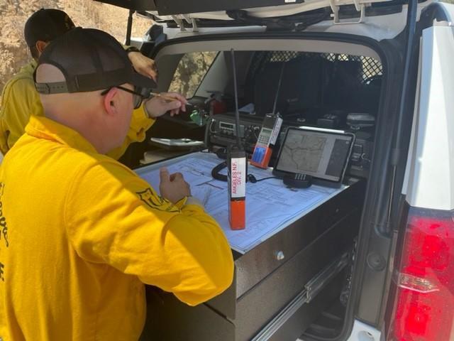 Fire managers in yellow shirts and ballcaps plan attack on a wildfire from the back of a vehicle.