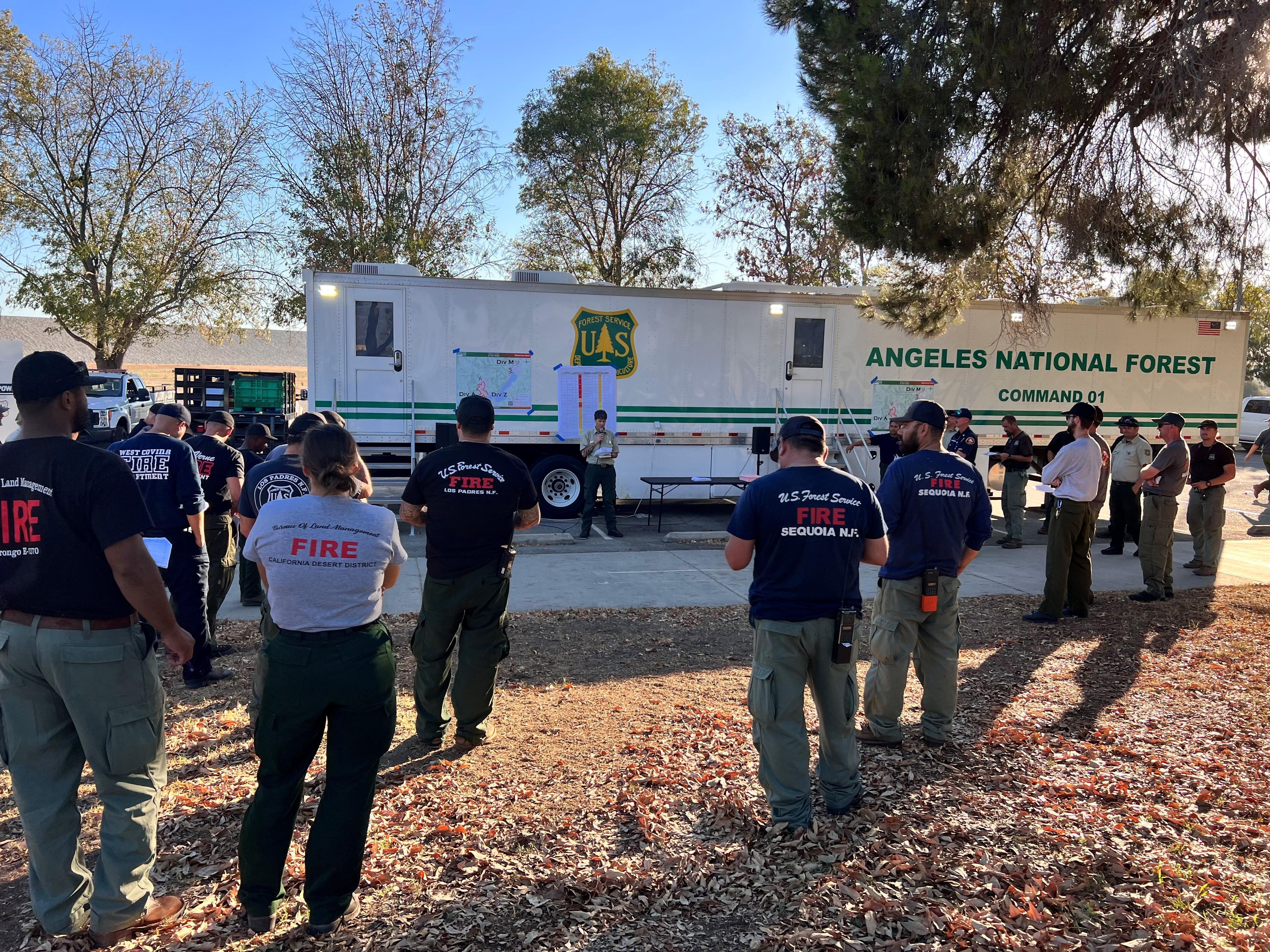 Multiple fire personnel attend evening fire briefing in front of Angeles National Forest incident command trailer
