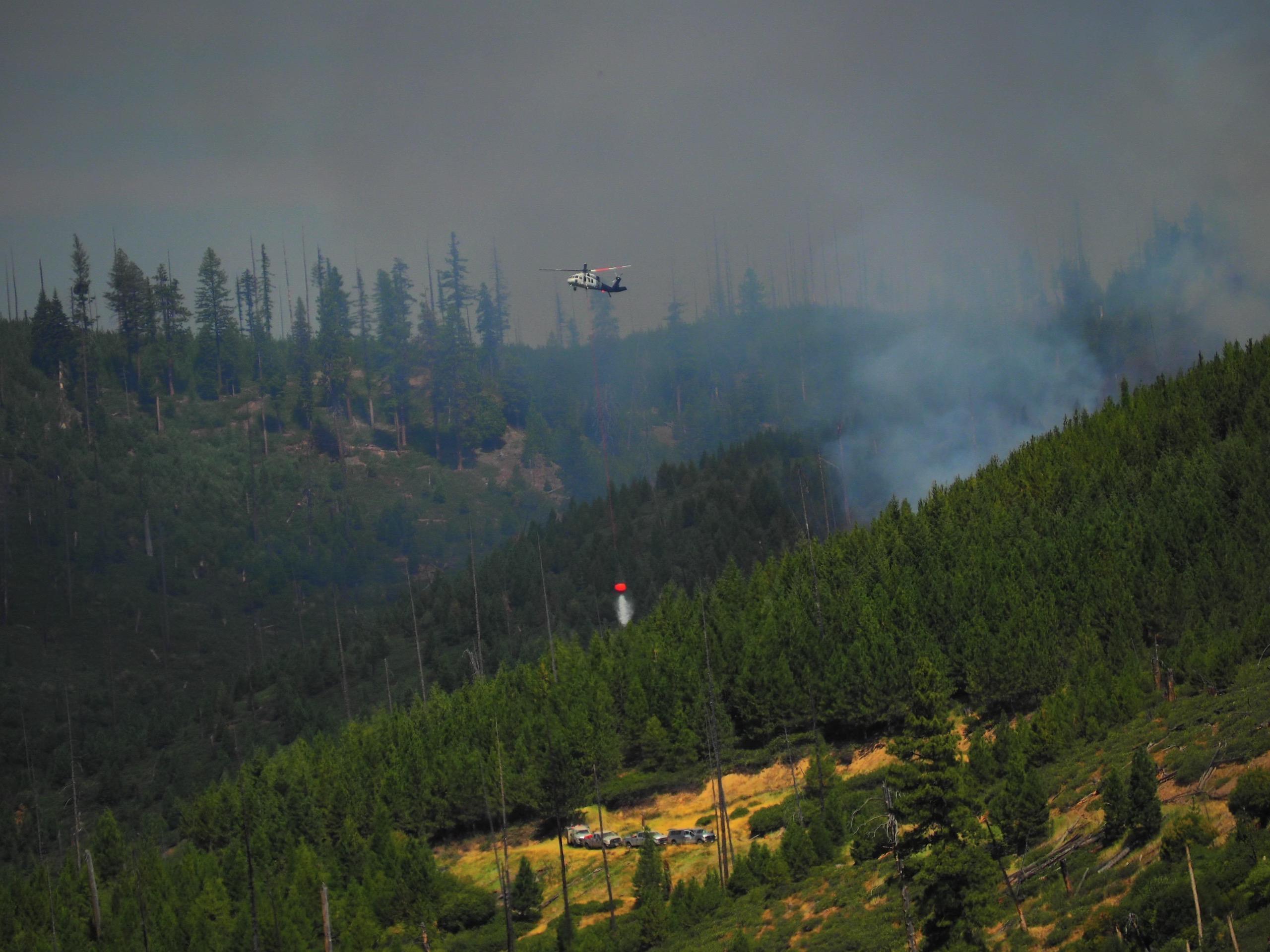 Helicopter cooling down fires edge to support ground crews