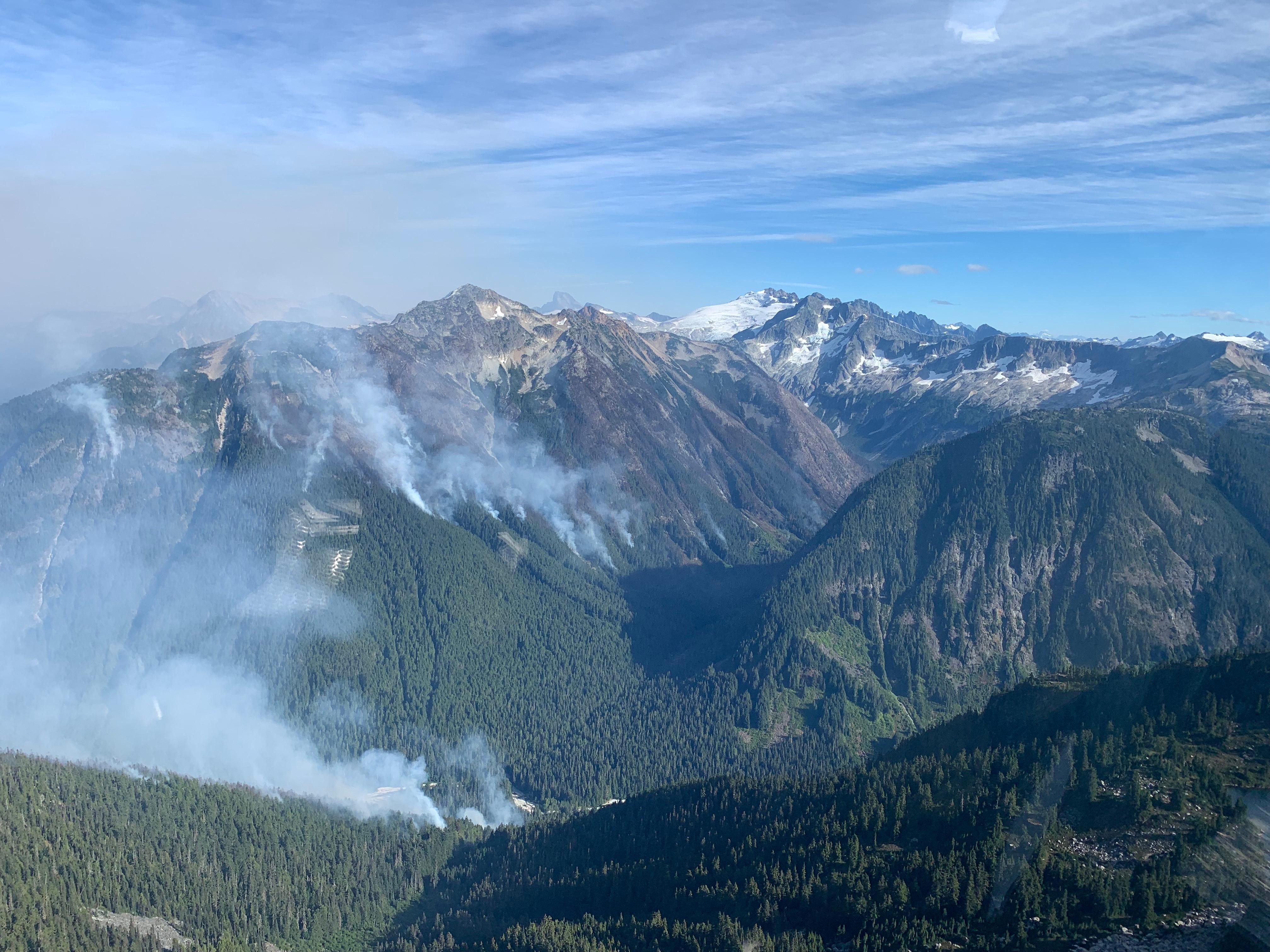 A number of white wispy smoke plumes rising off very steep terrain.