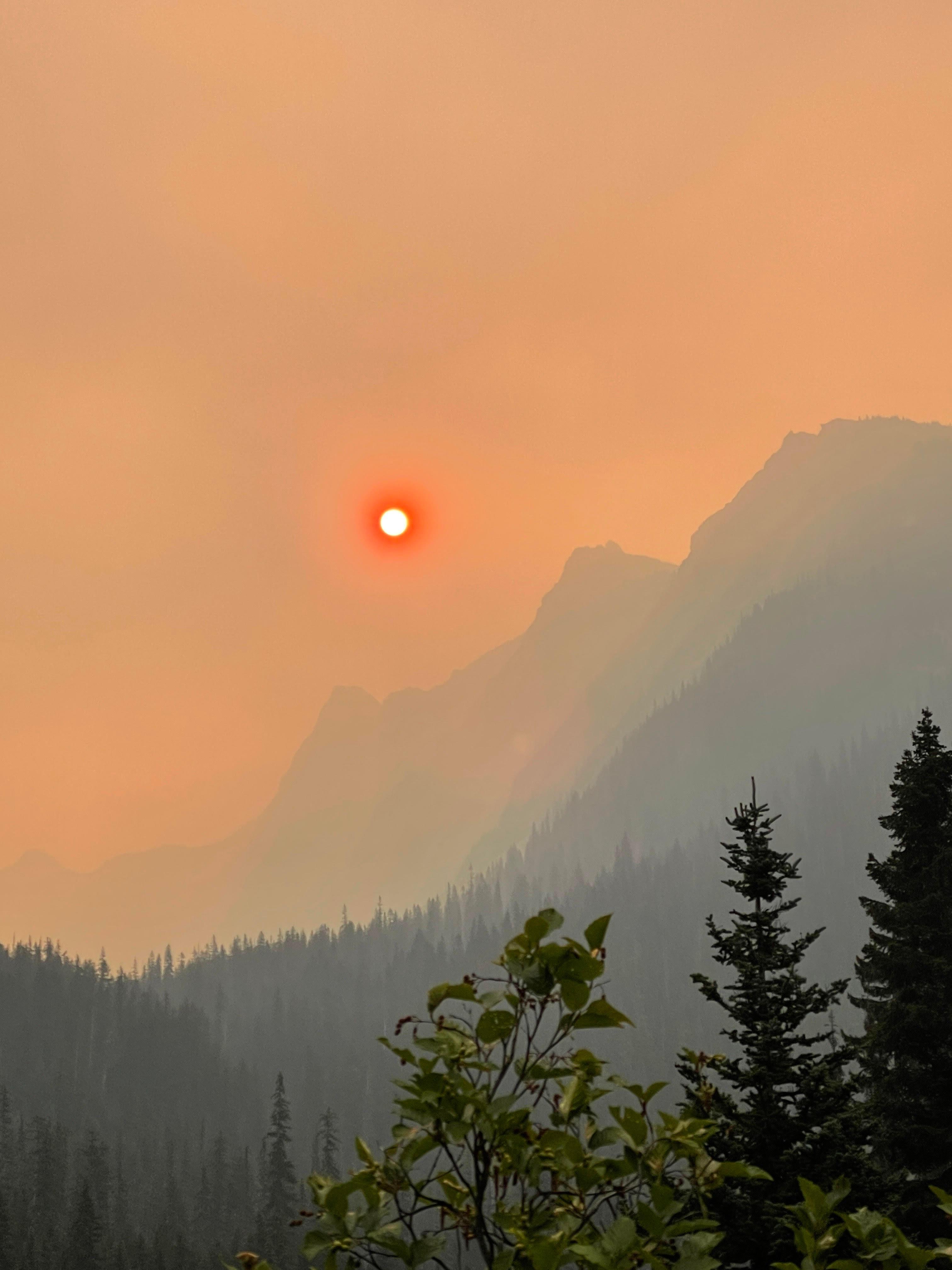 A mountain range silhouetted against a smoky sky. The sun is orange.