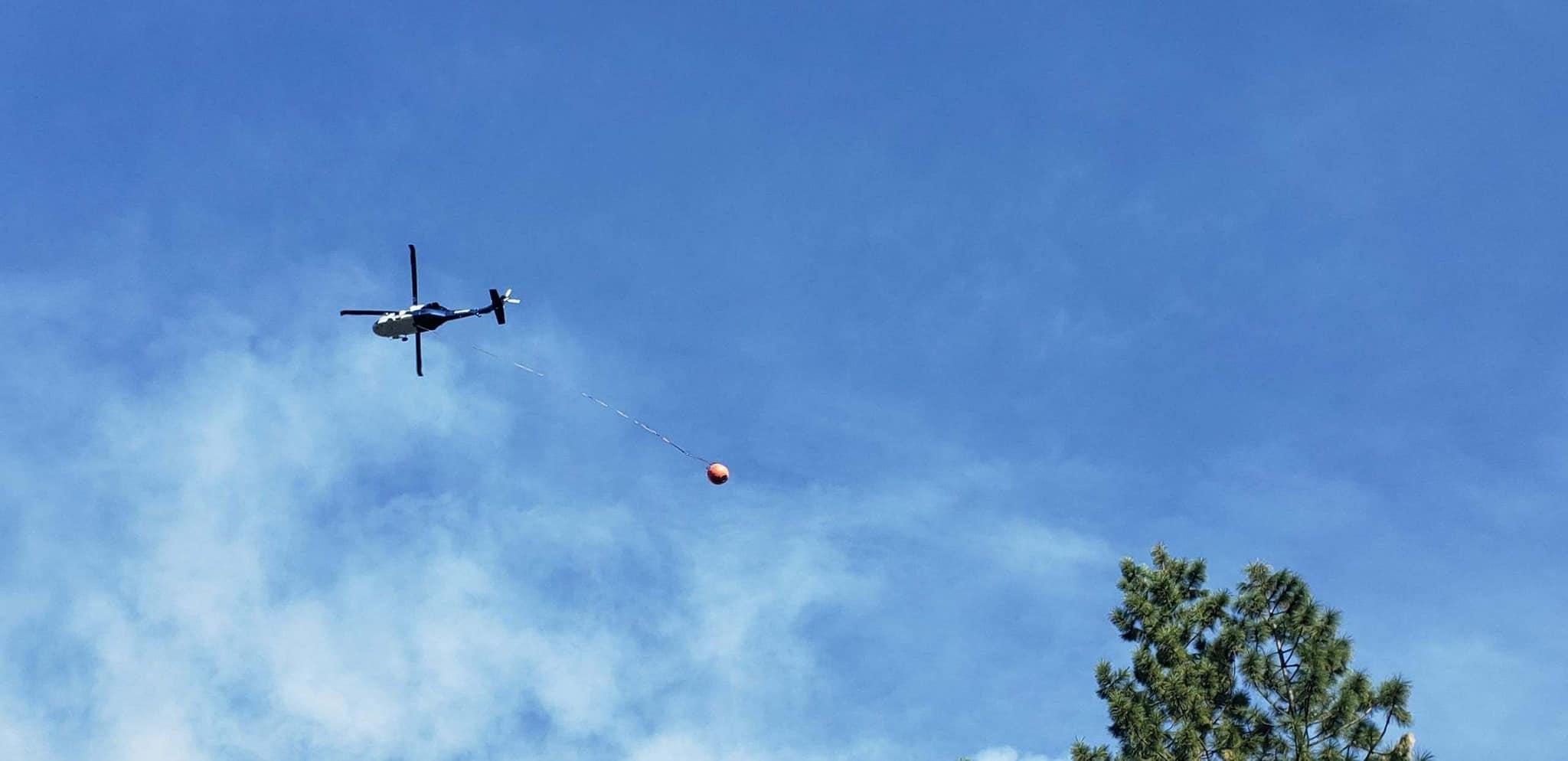 A helicopter carrying a water bucket works near Foresthill on the Mosquito Fire