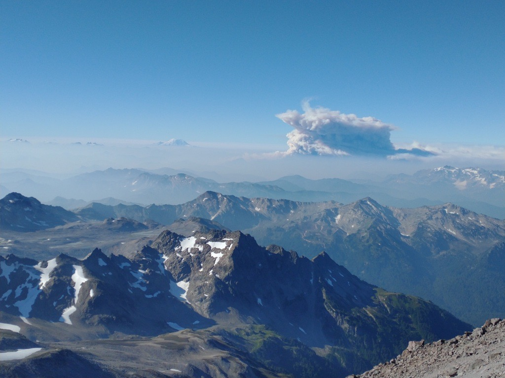 A smoke plume is seen from the distance from an adacent peak on a clear day.