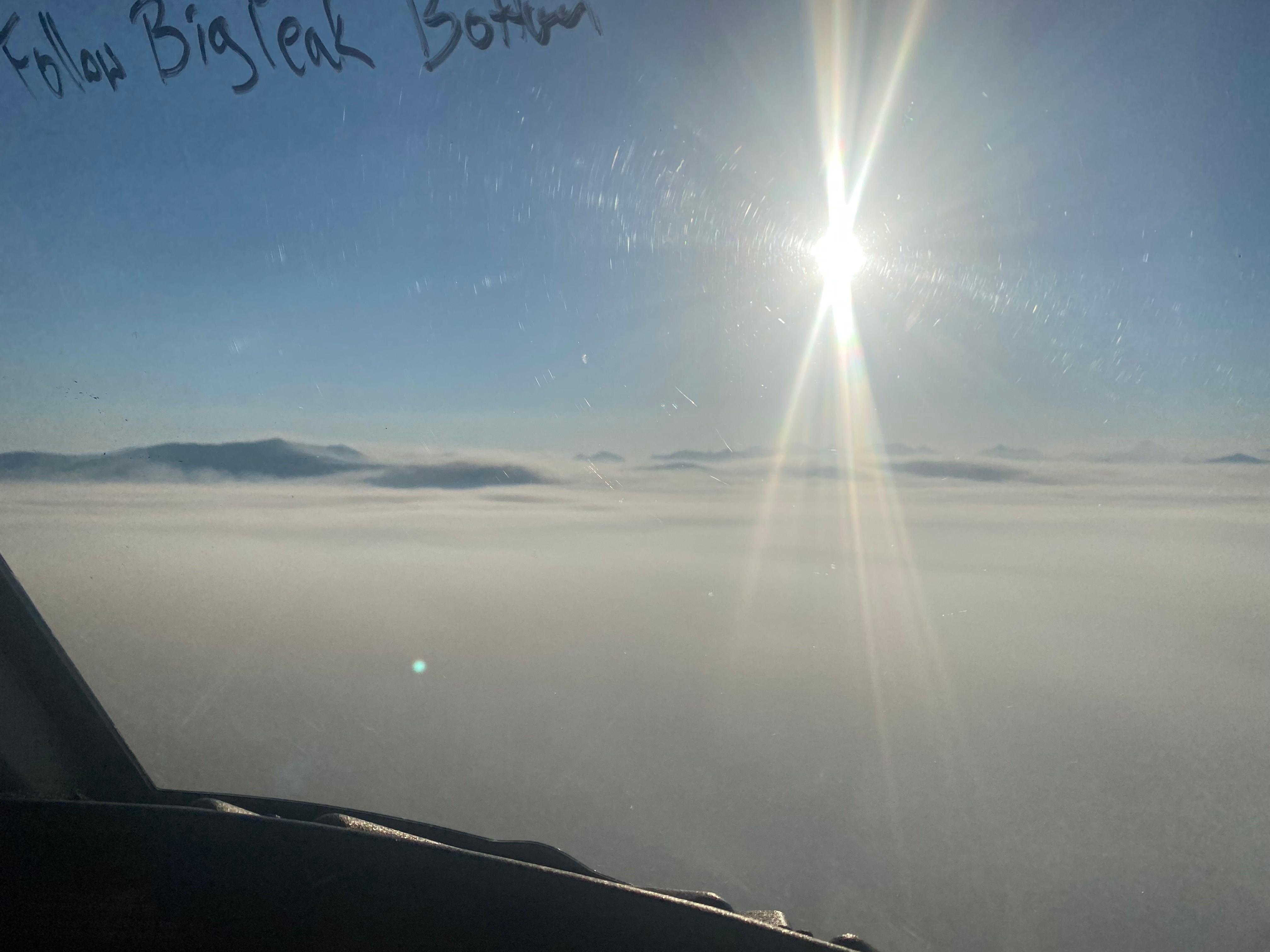 View thru helicopter windshield as it flies over smoke inversion