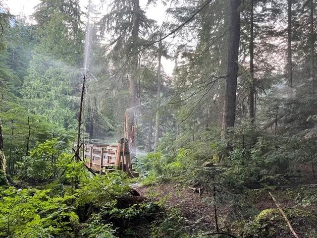 A manmade wooden structure in the forest with sprinklers attached and spraying water