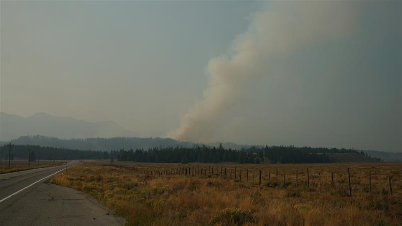 a smoke column rises in the distance and seen from Smiley Creek