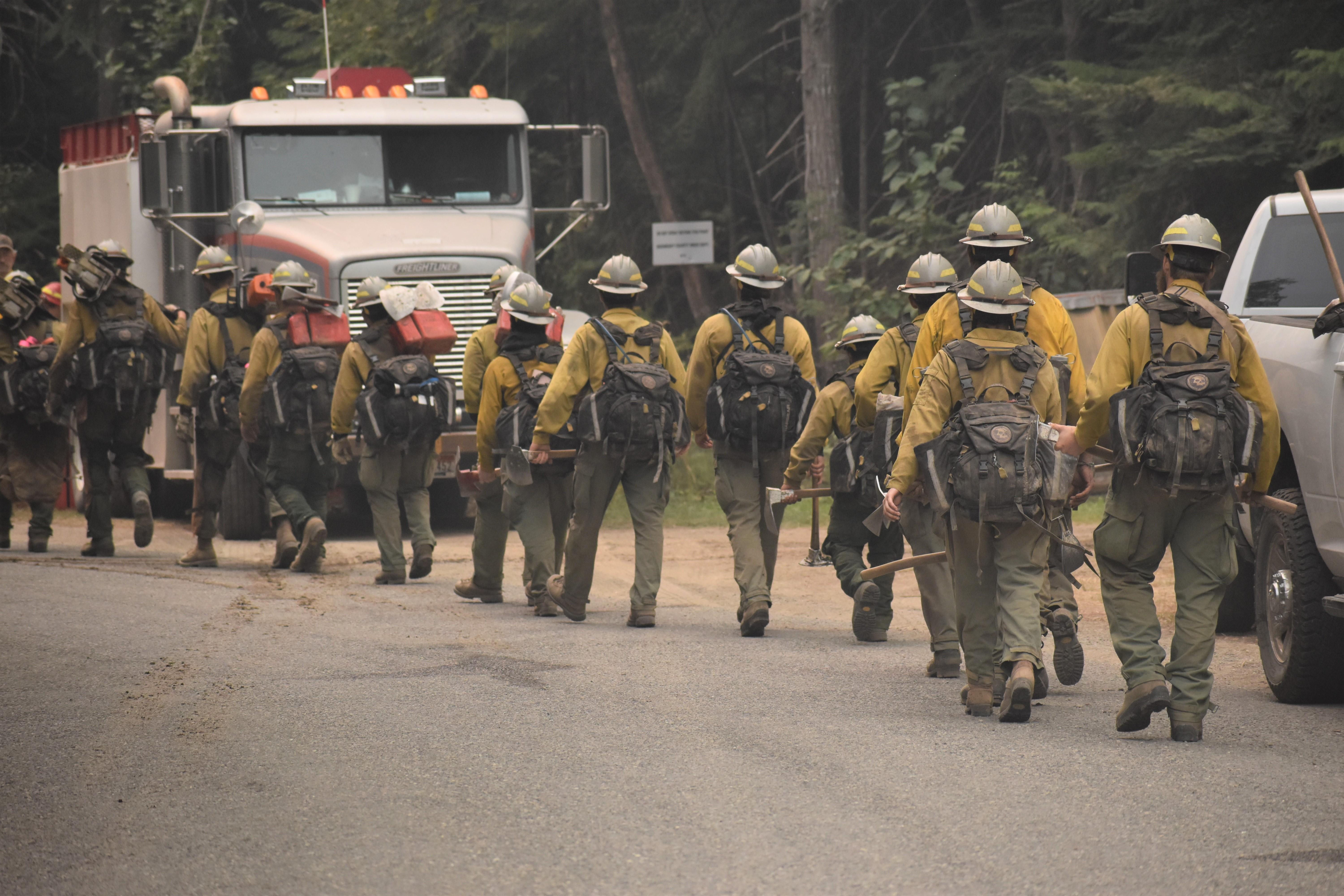 Firefighting crew hiking to fireline. Crew is hiking in line with their fire packs and tools past a water tender.
