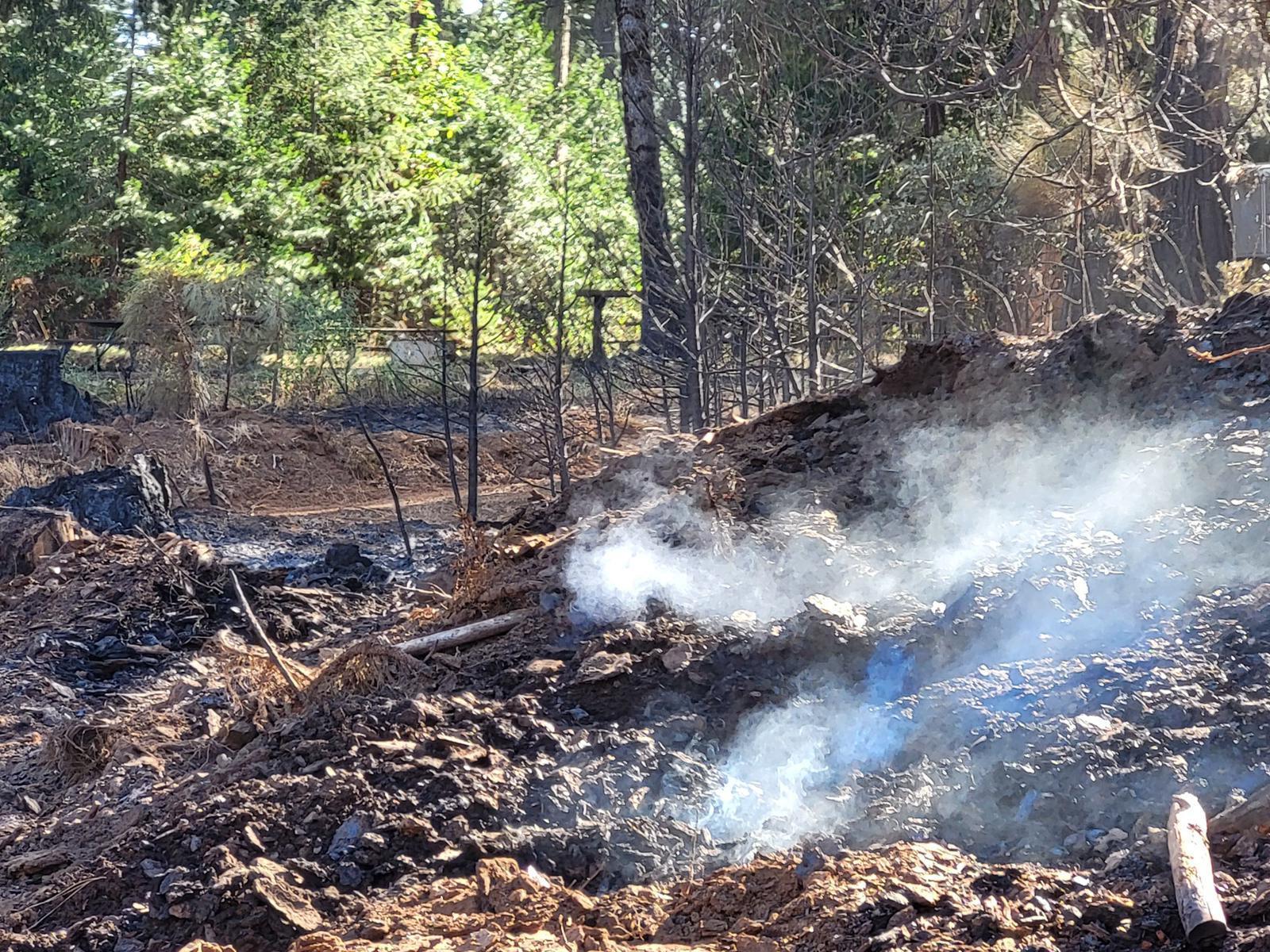 A smoldering rocky mound where a tree had been that remains a hazard in an evacuated area. Example of hazards that need to be eliminated before people can return home.