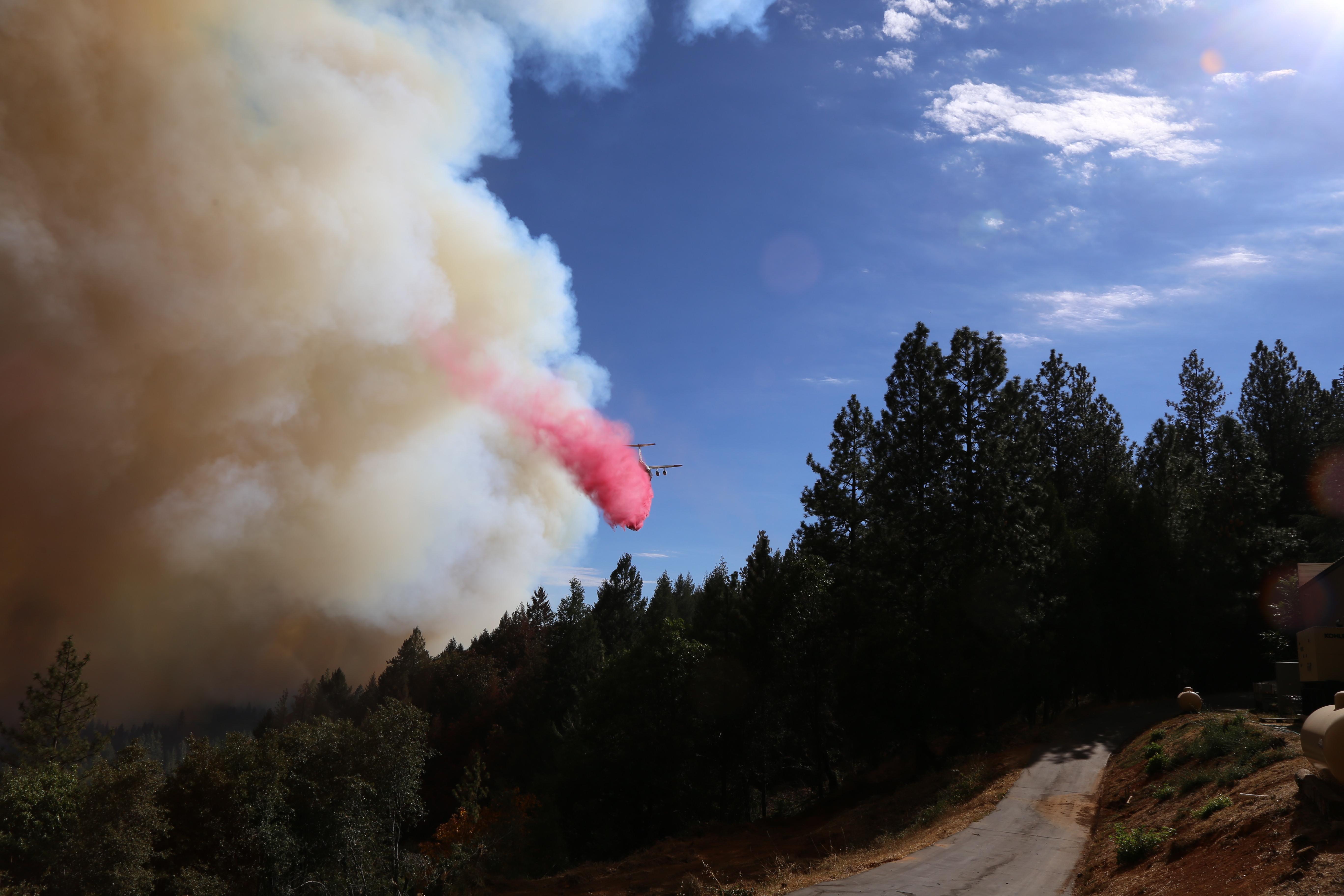 fixed-wing air tanker flying on the edge of thick wildfire smoke, dropping pink retardant on unburned trees