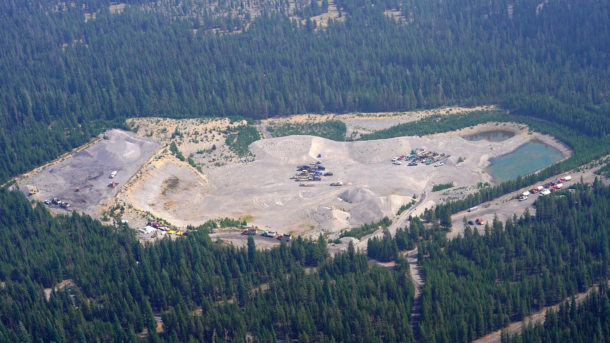 An aerial view of heavy equipment transport trucks with trailers parked in a sand and gravel pit.