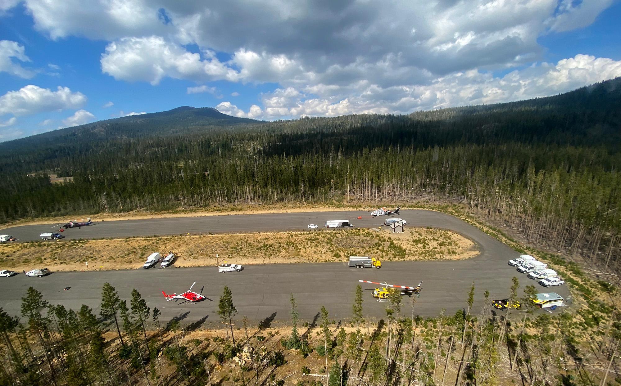 An aerial view of helicopters parked at a Sno-Park surrounded by pine trees.
