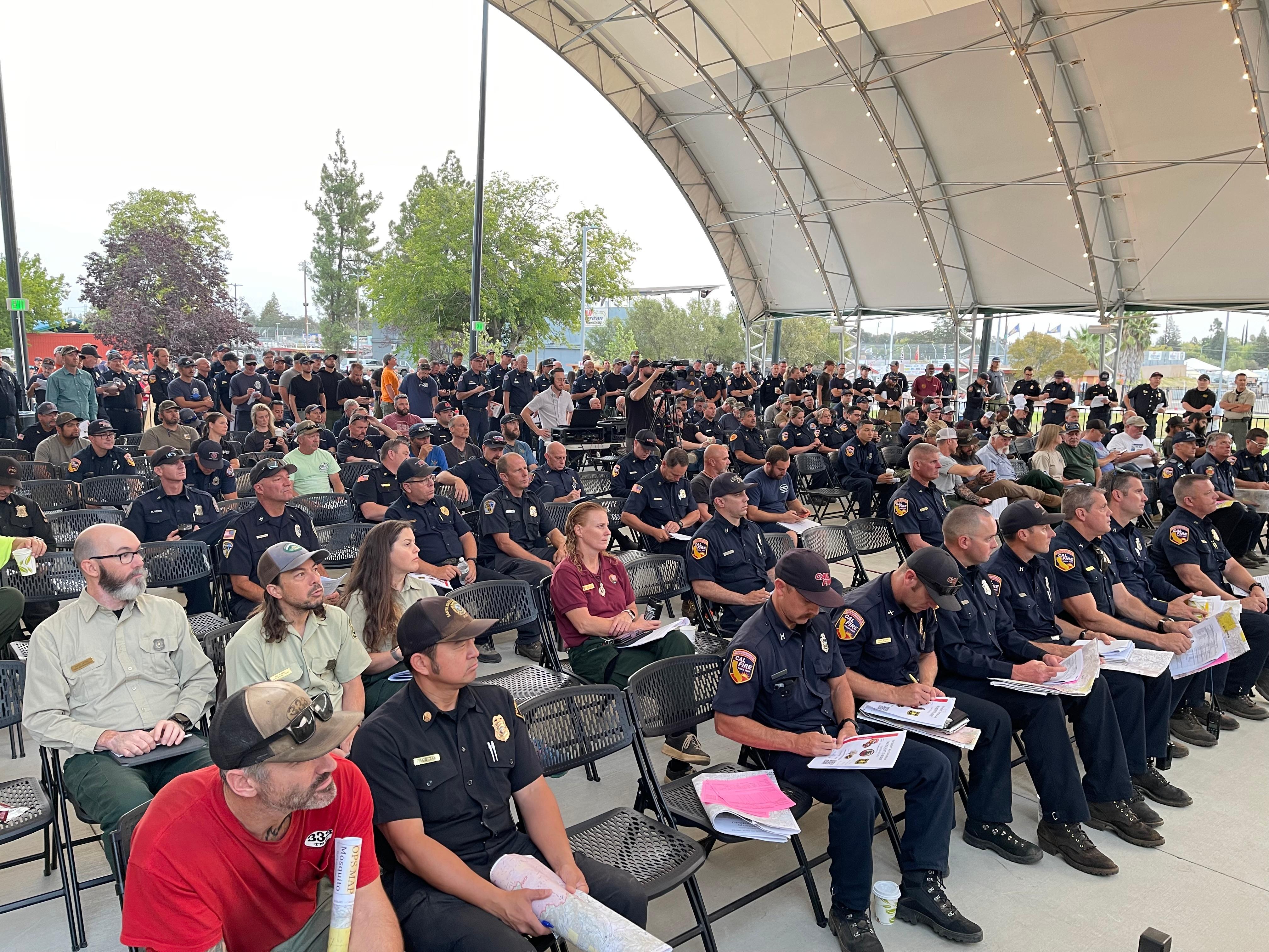dozens of fire personnel assembled in a large, partially open outdoor venue reflect during a nine eleven remembrance