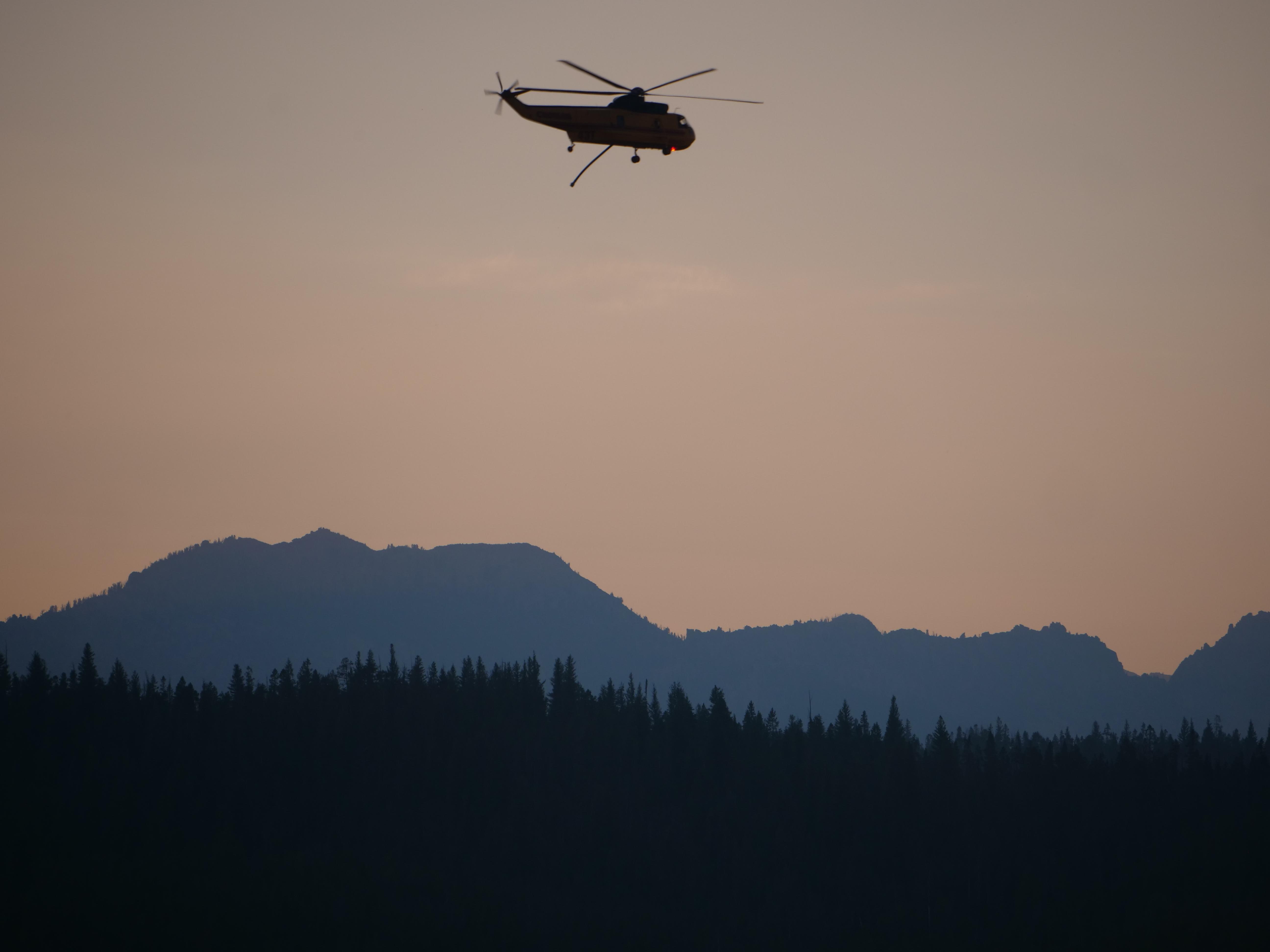A helicopter flies past mountains at sunset