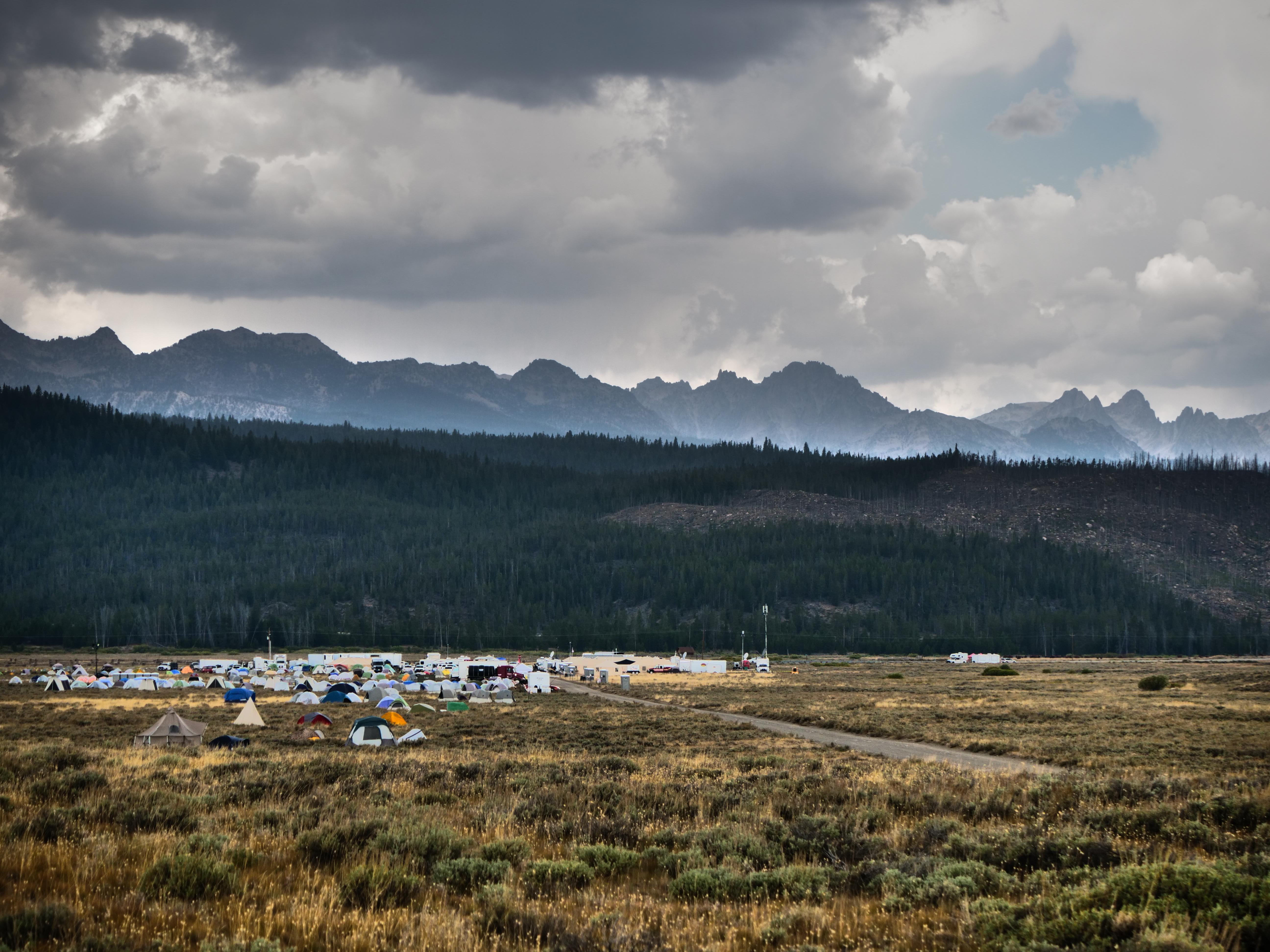 Mountains are seen in the distance with tents and a road in the foreground. The tents are of many colors and sit on a sagebrush covered plain.