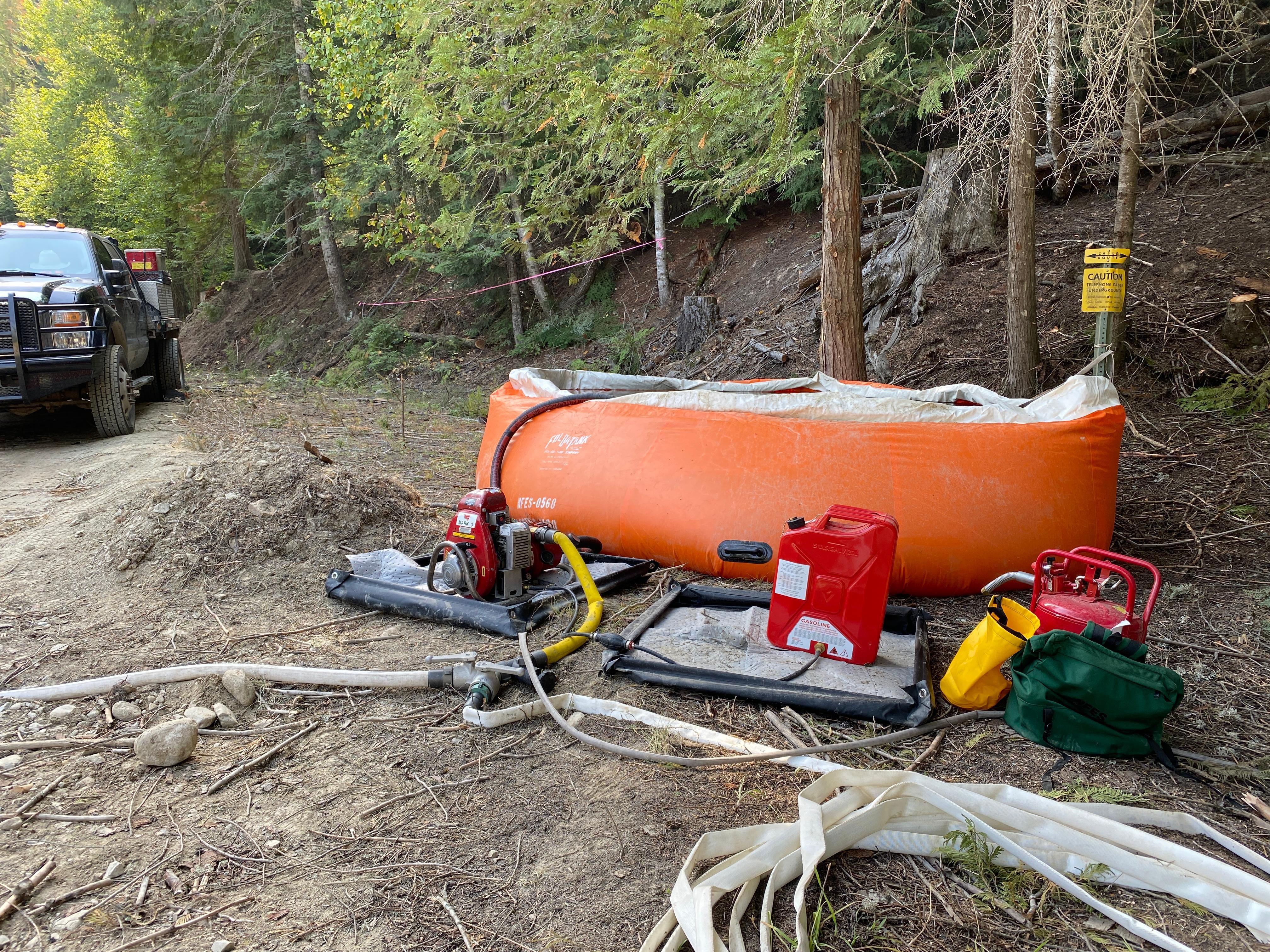 Portable water and pump for structure protection. Fire engine in driveway next to a orange water container with pump and hose. 