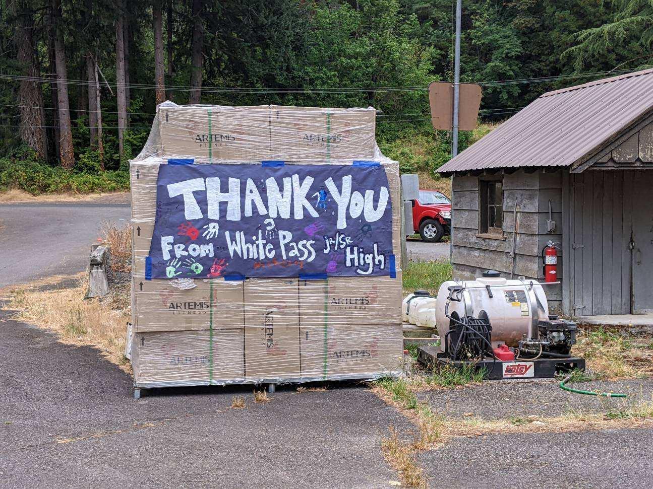 A purple sign with a thank you note from White Pass Jr./Sr. High School. On the poster are multiple hand prints and other painted items. The sign is hanging on a pallet of boxes sitting in the forest work yard at the Cowlitz Valley Ranger District.