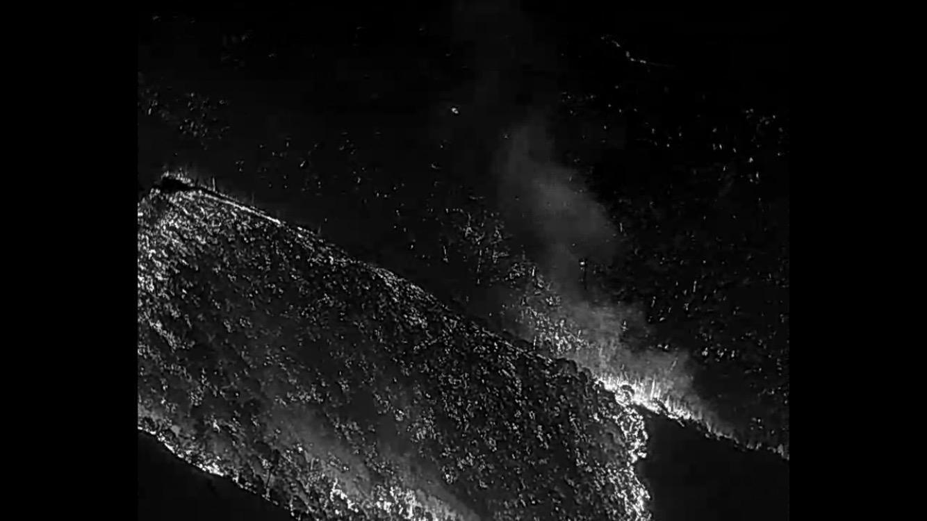 Dark, almost black outline and shape of mountains with a bright white contrasting surface of the hillside where the fire's heat is revealed with infrared imagery cameras