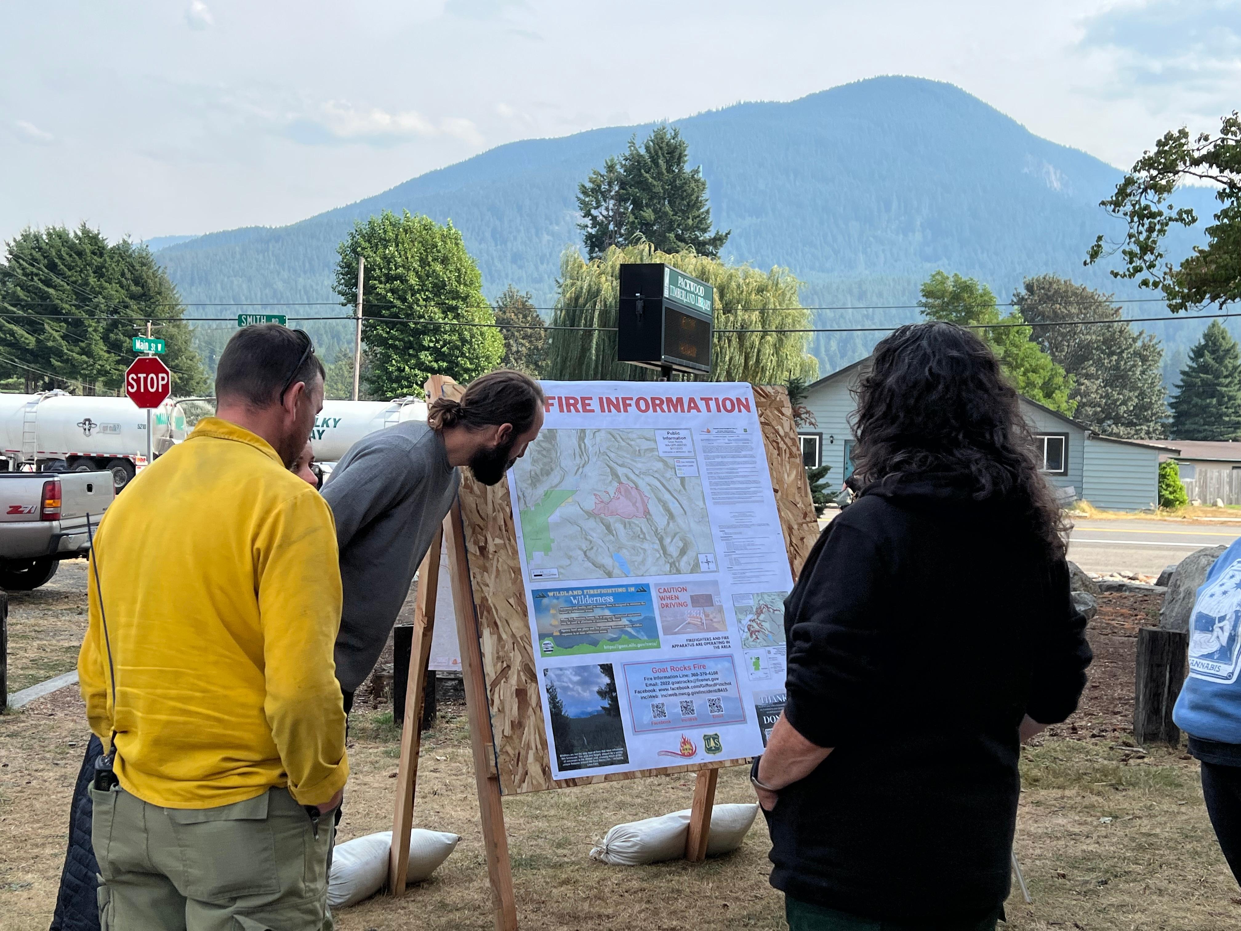 Members of the public stop and talk with a Public Information Officer at an Information board. The board was set up for the Packwood Farmer's Market to inform and answer questions anyone may have.