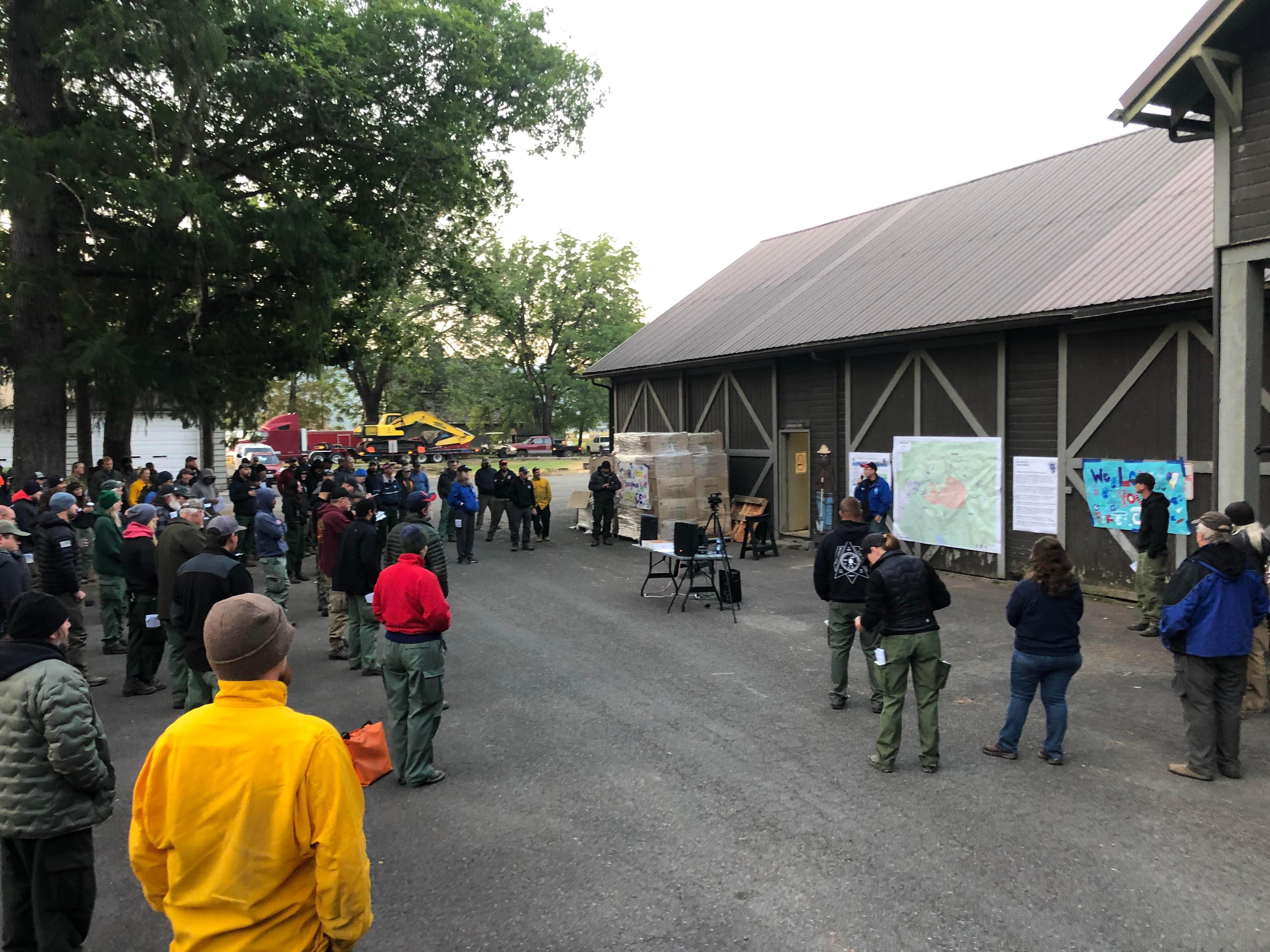 Fire personnel gather by a building where a large map of the fire is posted. Fire managers are briefing them on what is happening on the fire, the weather, assignments for the day, and other important information.