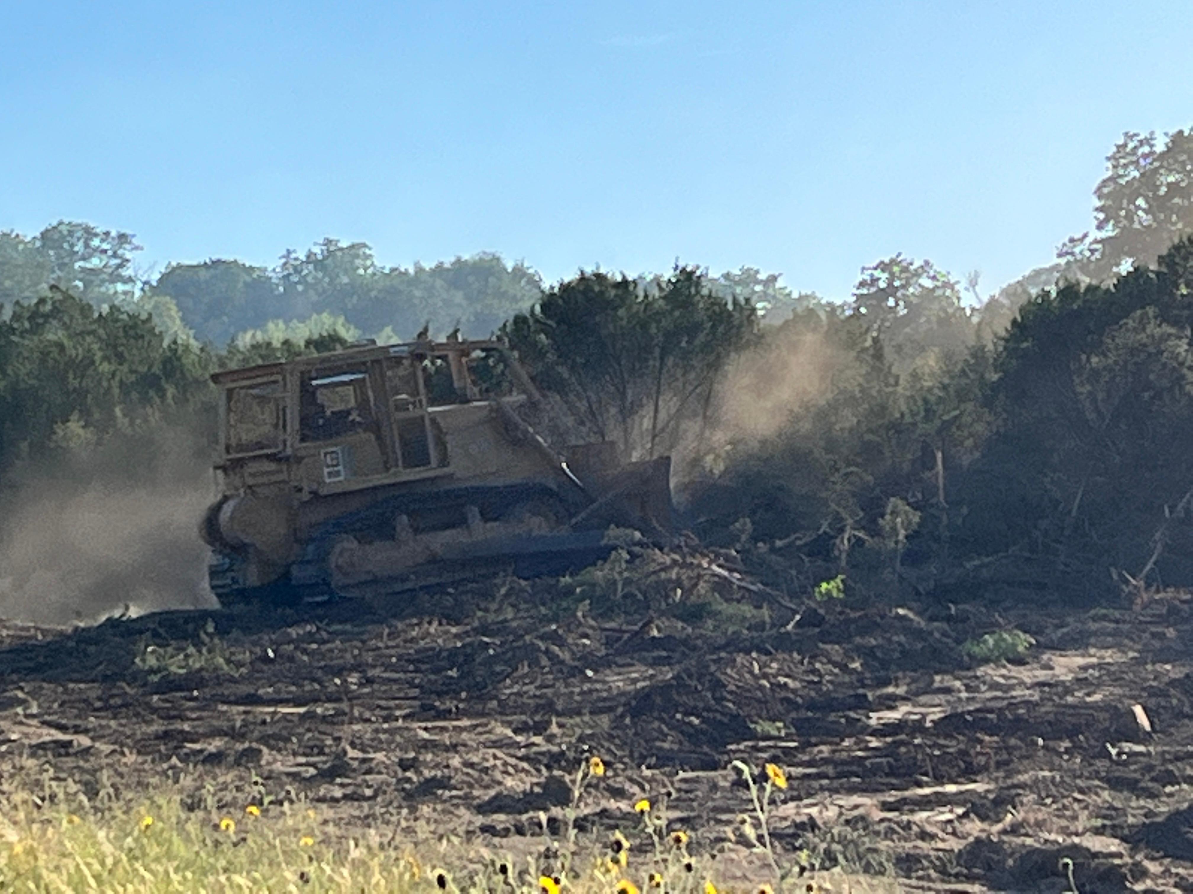 This picture shows an area that has been worked by a dozer clearing trees. the dozer is also shown pushing more trees to widen the area