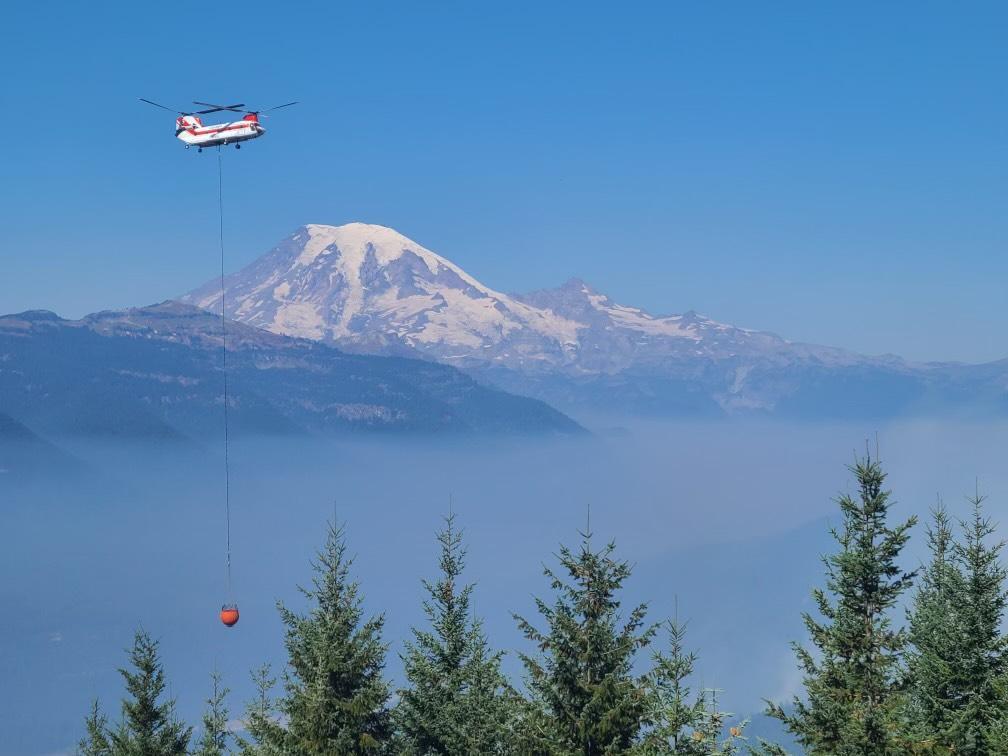 A Type 1 helicopter flyer over wildfire smoke with Mount Ranier in the background