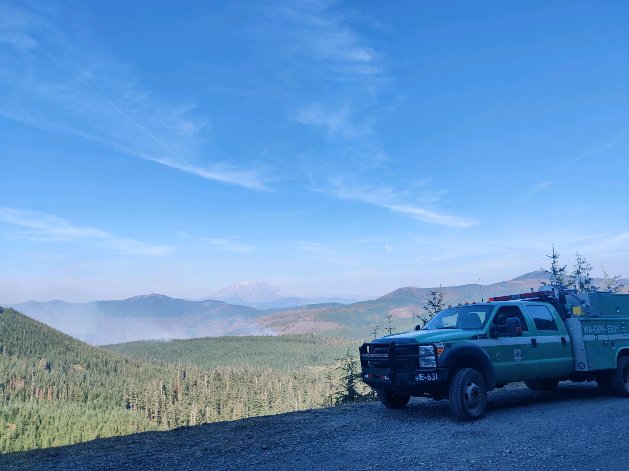 A fire engine on a ridge above Siouxon Fire- smoke is seen in the distance among the green forest below