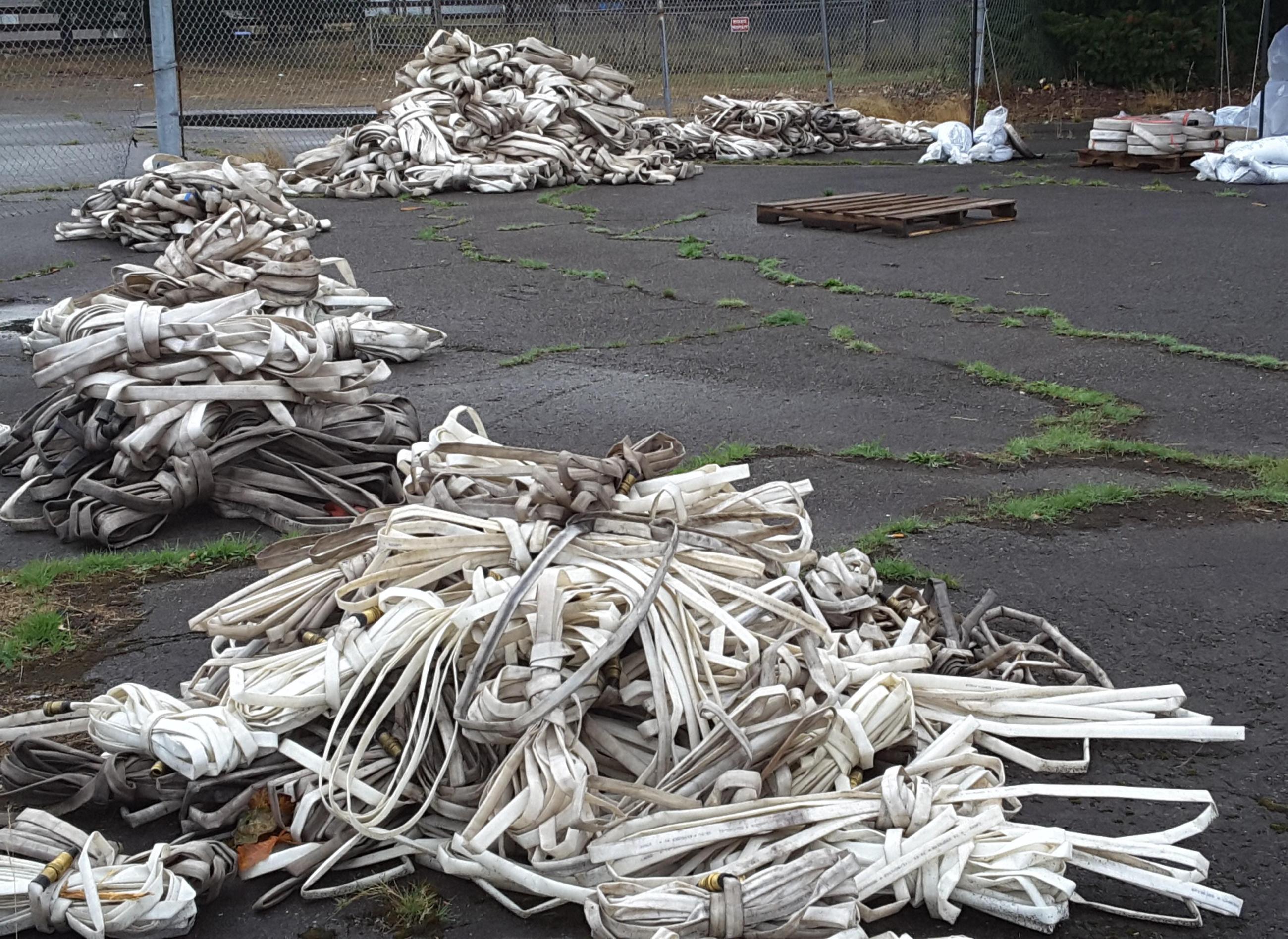 Multiple piles of dirty fire hose are stacked along the fence in a parking lot.