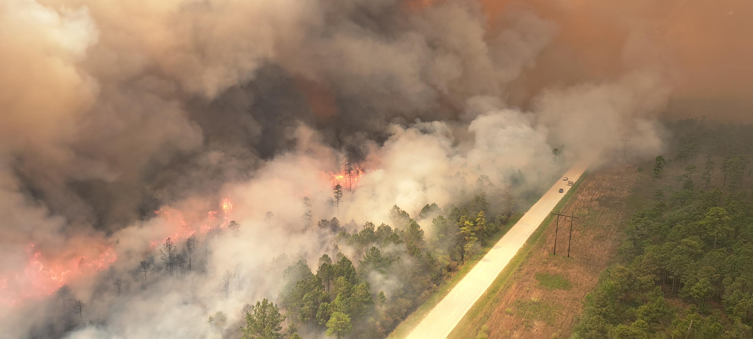 Fire activity and smoke shows along a roadway on the Great Lakes Fire on April 21, 2023