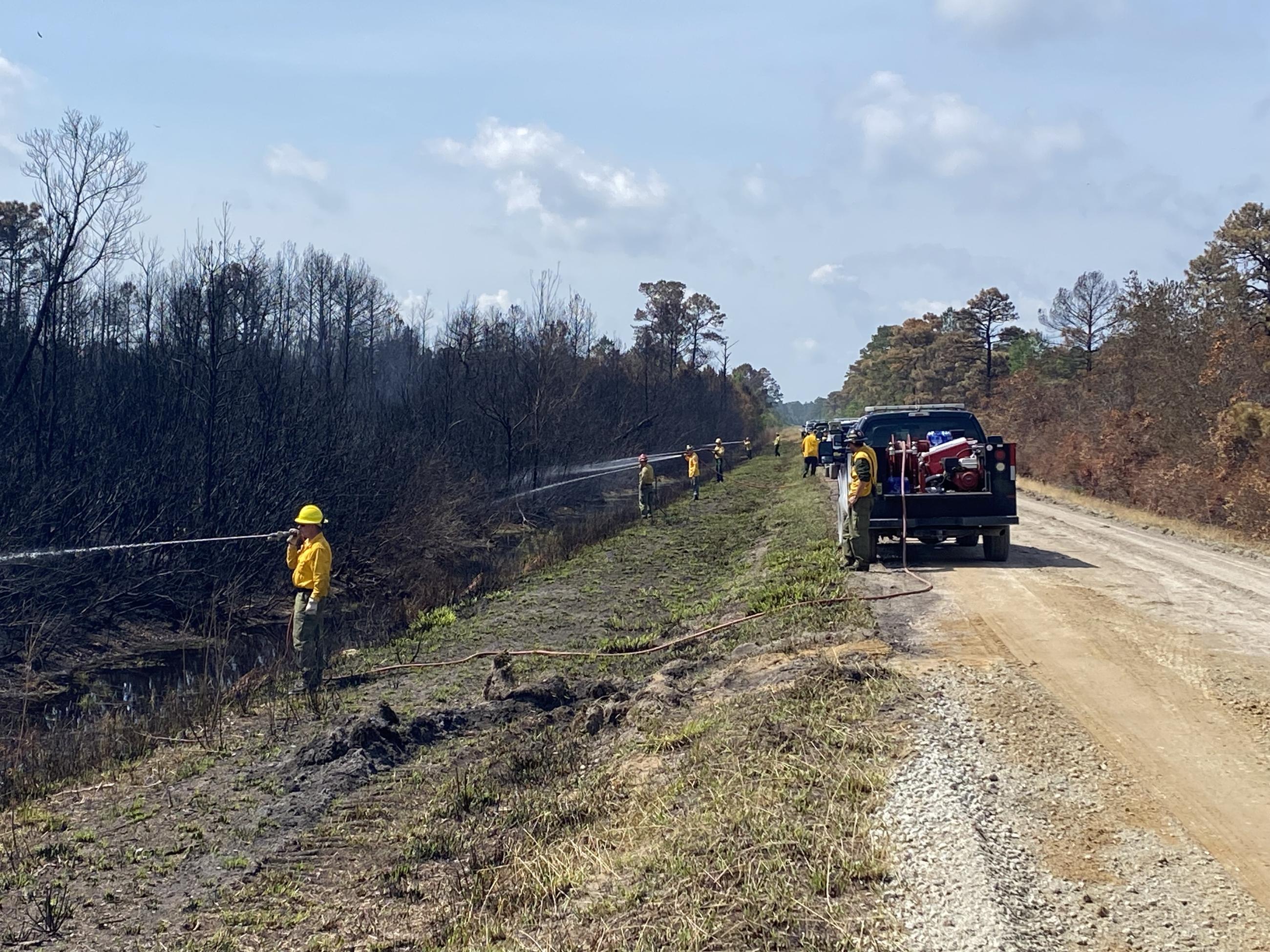 Engine Strike Team conducts mop-up operations on the Great Lakes Fire on April 29, 2023. Several engines line the roadways and firefighters man hose to spray burned areas with water.
