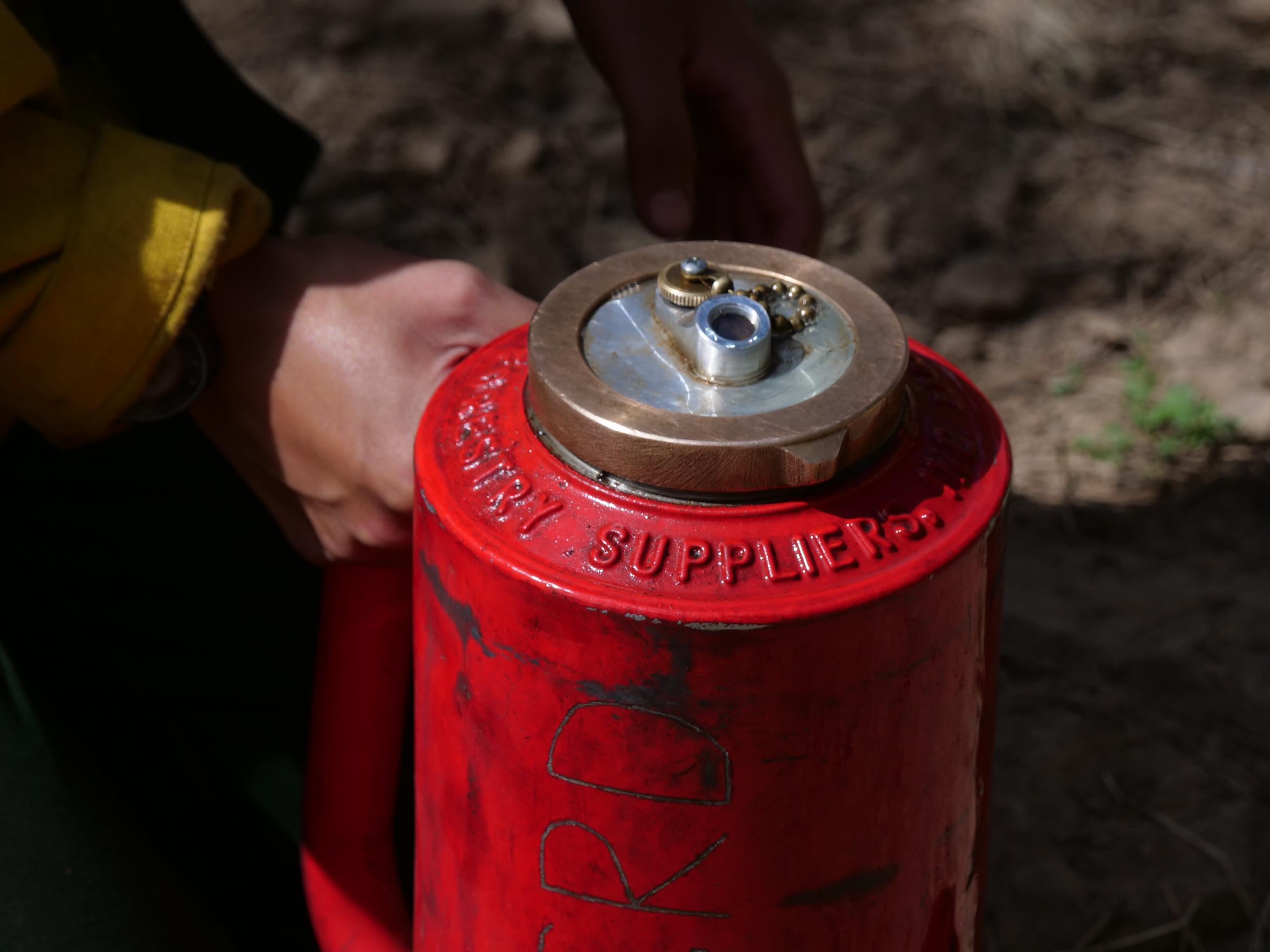 A red fuel can is shown being gripped by a firefighter's hand.